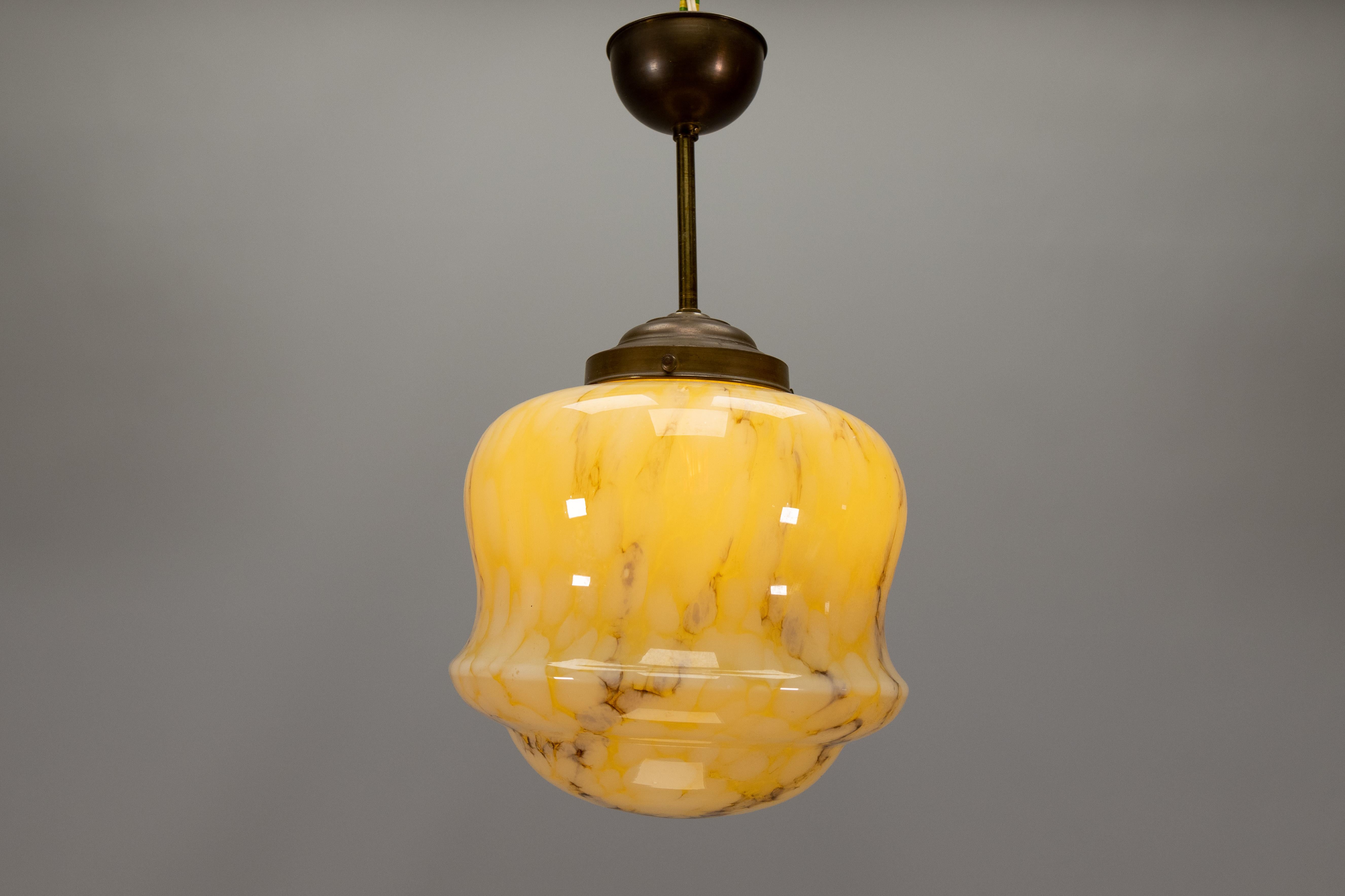 Una scultorea lampada a sospensione Art Déco degli anni '30, caratterizzata da un sorprendente paralume in vetro marmorizzato nei toni caldi dell'ambra e dell'avorio. Il motivo della superficie imita la pietra naturale con venature morbide e