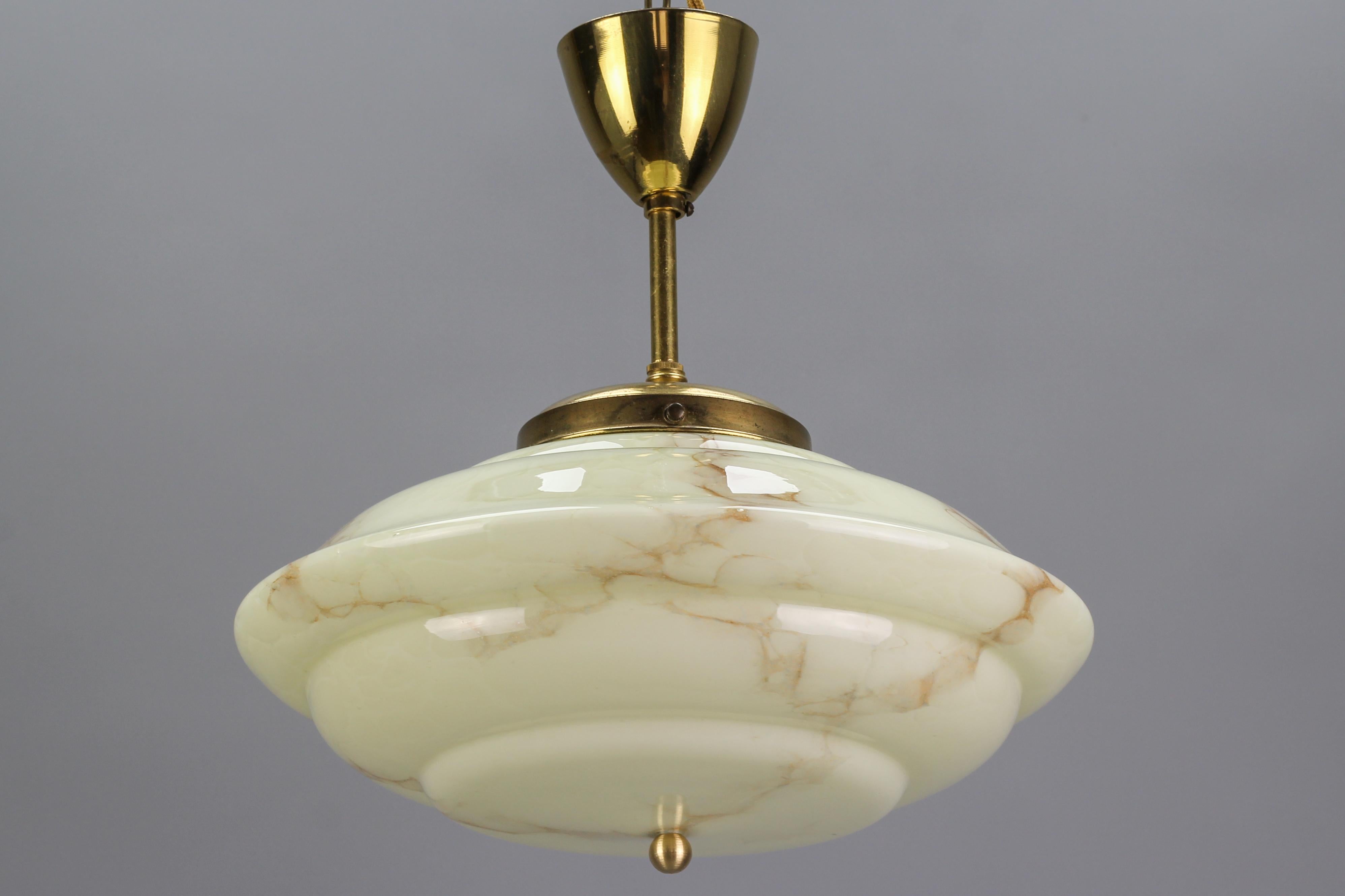 Adorable Art Deco cream and vanilla - beige-colored marbled/veined glass pendant ceiling lamp. Ufo-shaped glass lampshade; brass rod and canopy. 
The lamp fits in a 1930s style interior as well as a modern interior, especially suitable for a lower