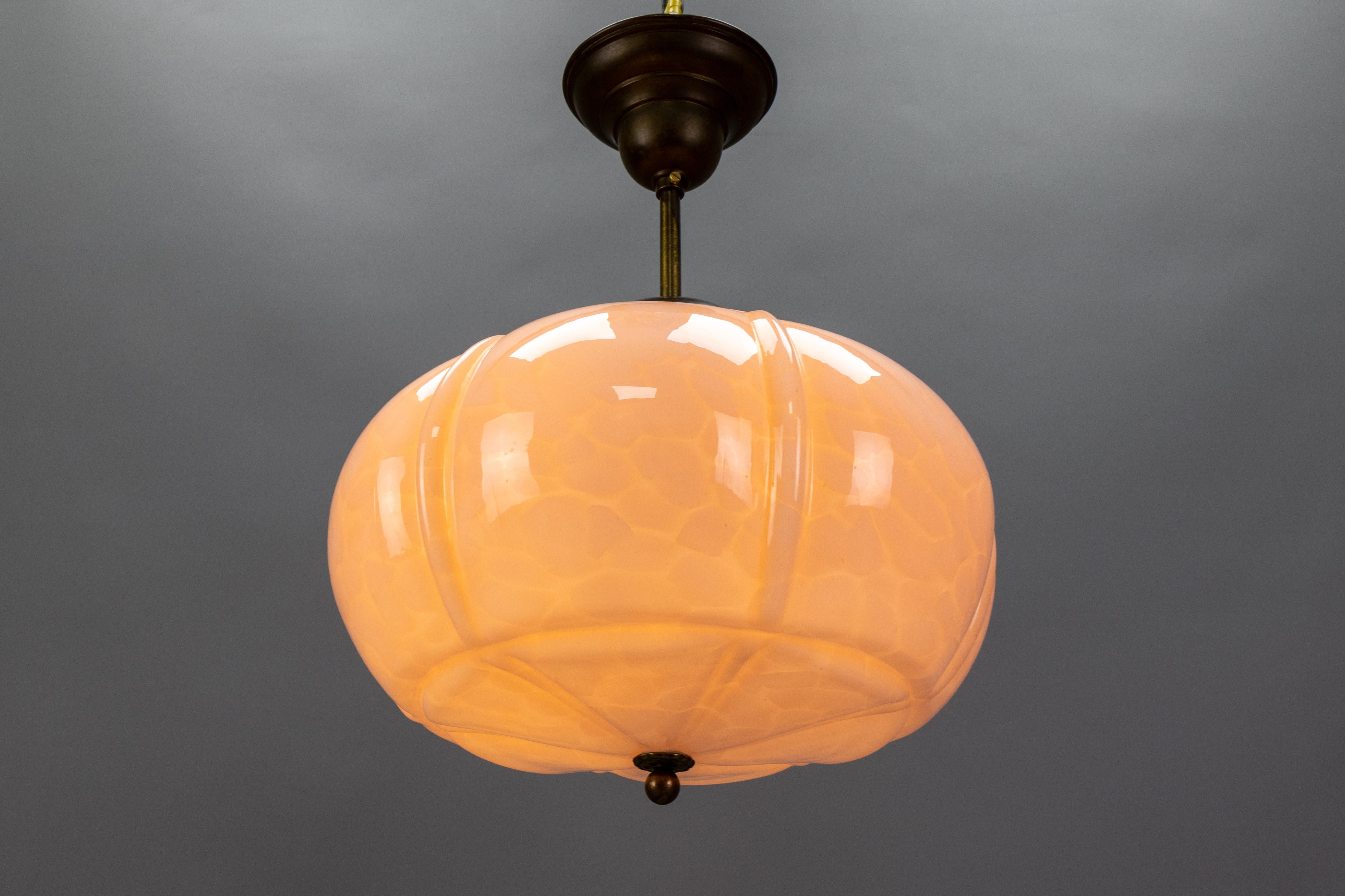 An Art Deco marbled light pink glass and brass pendant light from the 1930s, Germany. 
This adorable ceiling fixture features a beautifully shaped, light pink marbled glass shade with a brass finial. It is suspended from a brass canopy and features