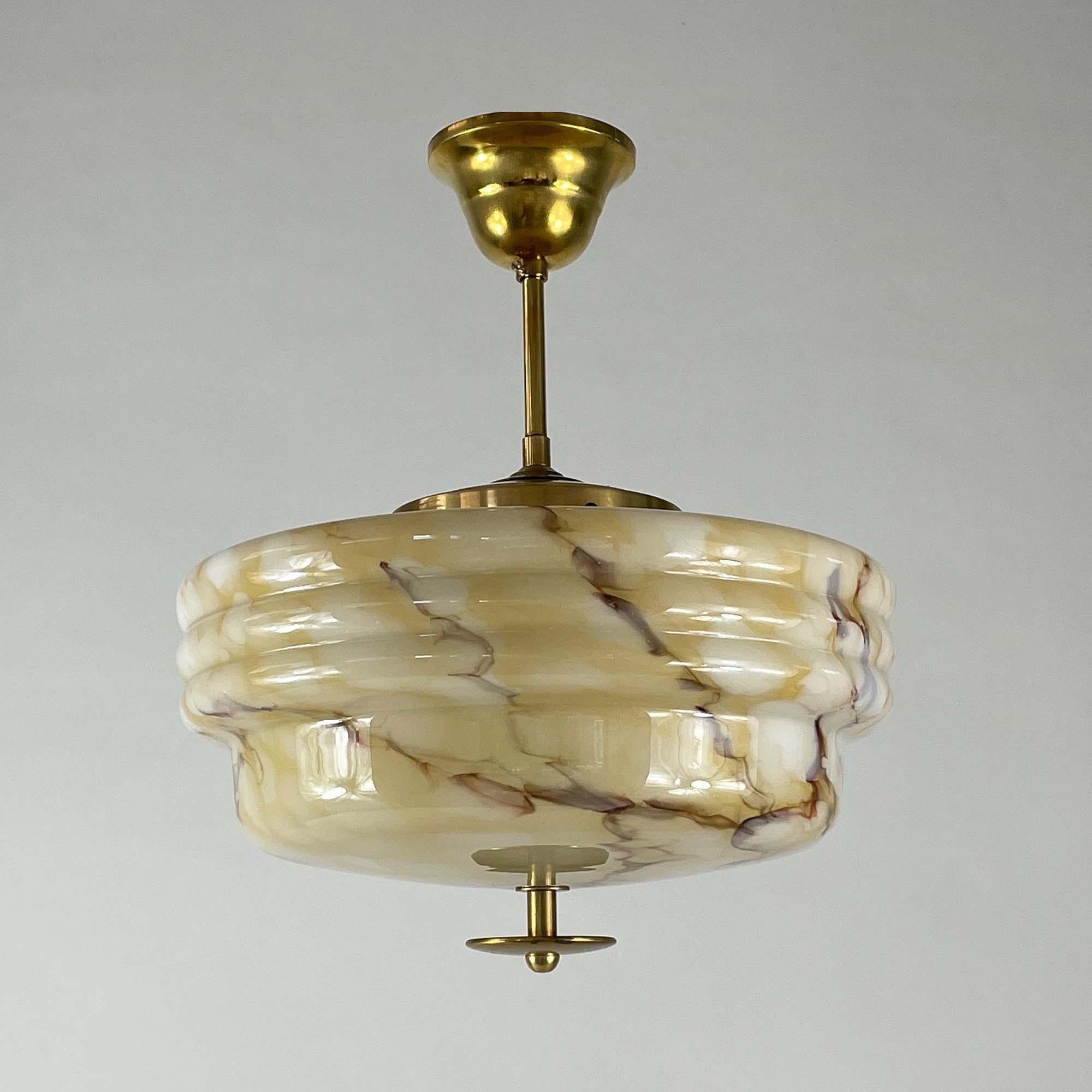 This minimalist Art Deco semi flush mount was designed and manufactured in Germany in the 1930s during the Bauhaus era. It features a rounded shade and brass hardware. The shade is made of sand, yellowish, beige and brown colored marbled opaline