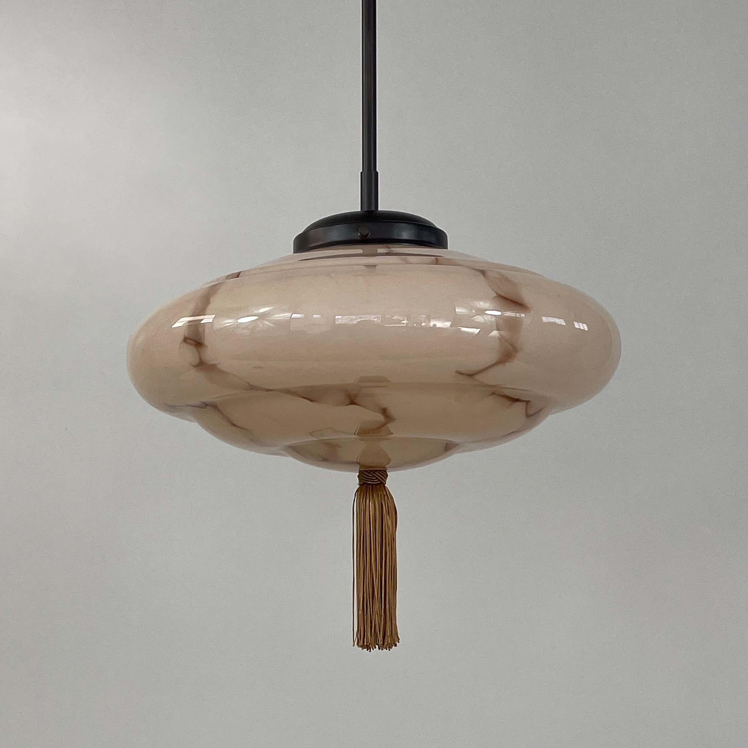 This unusual Art Deco fixture was designed and manufactured in Germany in the 1920s to 1930s during the Bauhaus period. It features a cream colored marbled glass lampshade, a bronze silk tassel and bronzed brass hardware. The glass shade with a