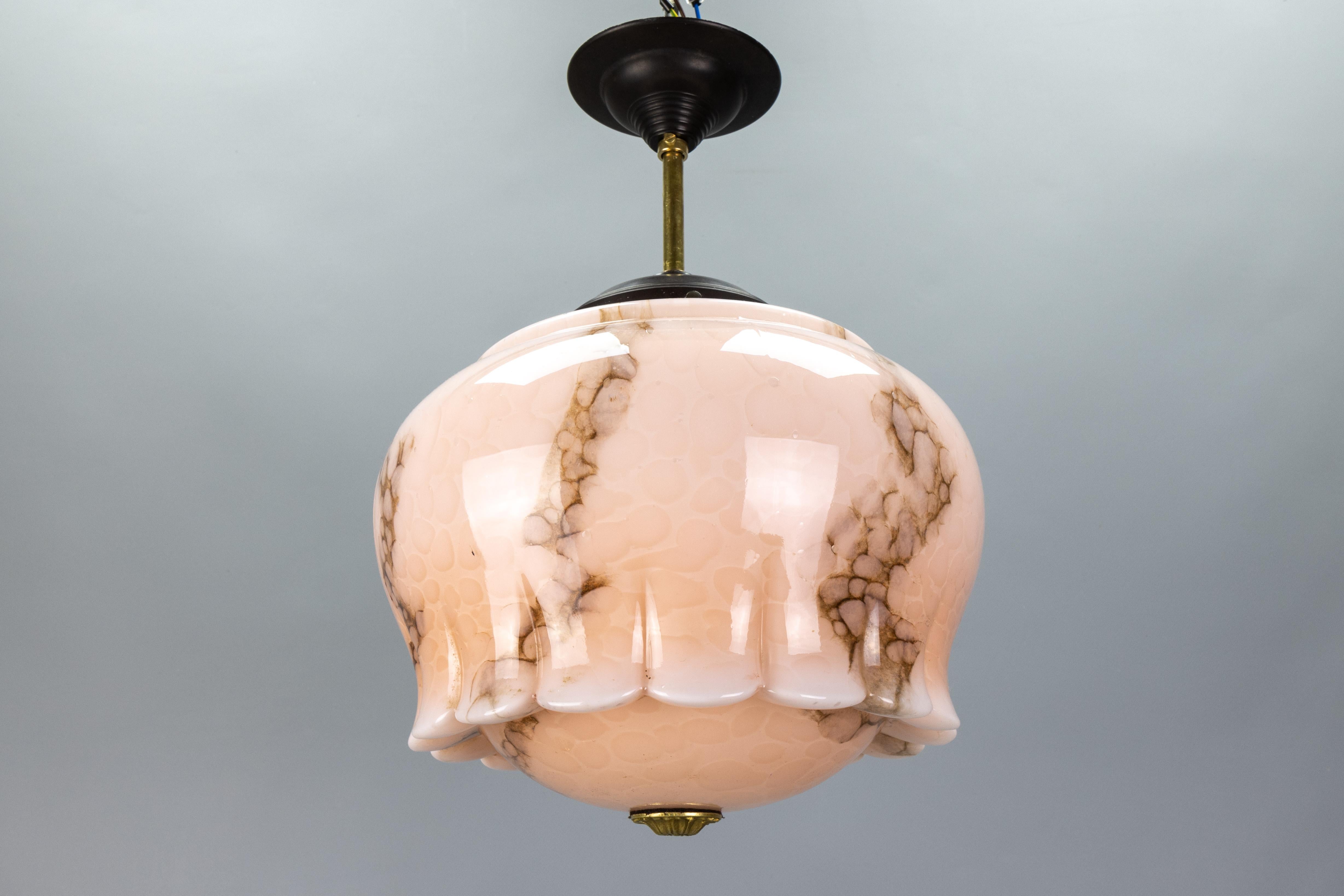 An Art Deco marbled pale pink and brown glass, bakelite, and brass pendant light from the 1930s, Germany. 
This adorable ceiling light fixture showcases a marbled, beautifully shaped glass shade in pale pink with brown veins. The glass shade is