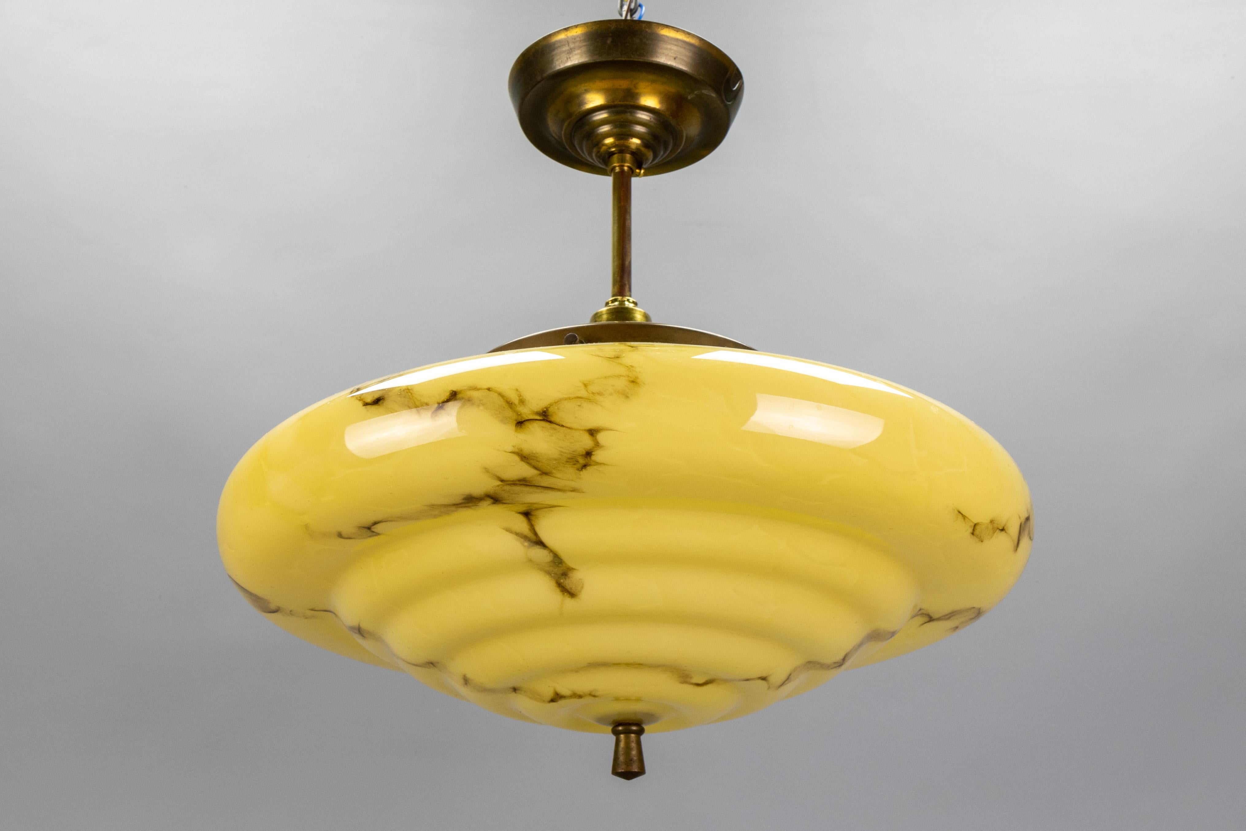 An Art Deco marbled, slightly layered dark yellow and brown glass and brass pendant light from the 1930s, Germany. 
This stunning ceiling light fixture showcases a marbled, slightly layered glass shade in dark yellow with brown veins. The glass