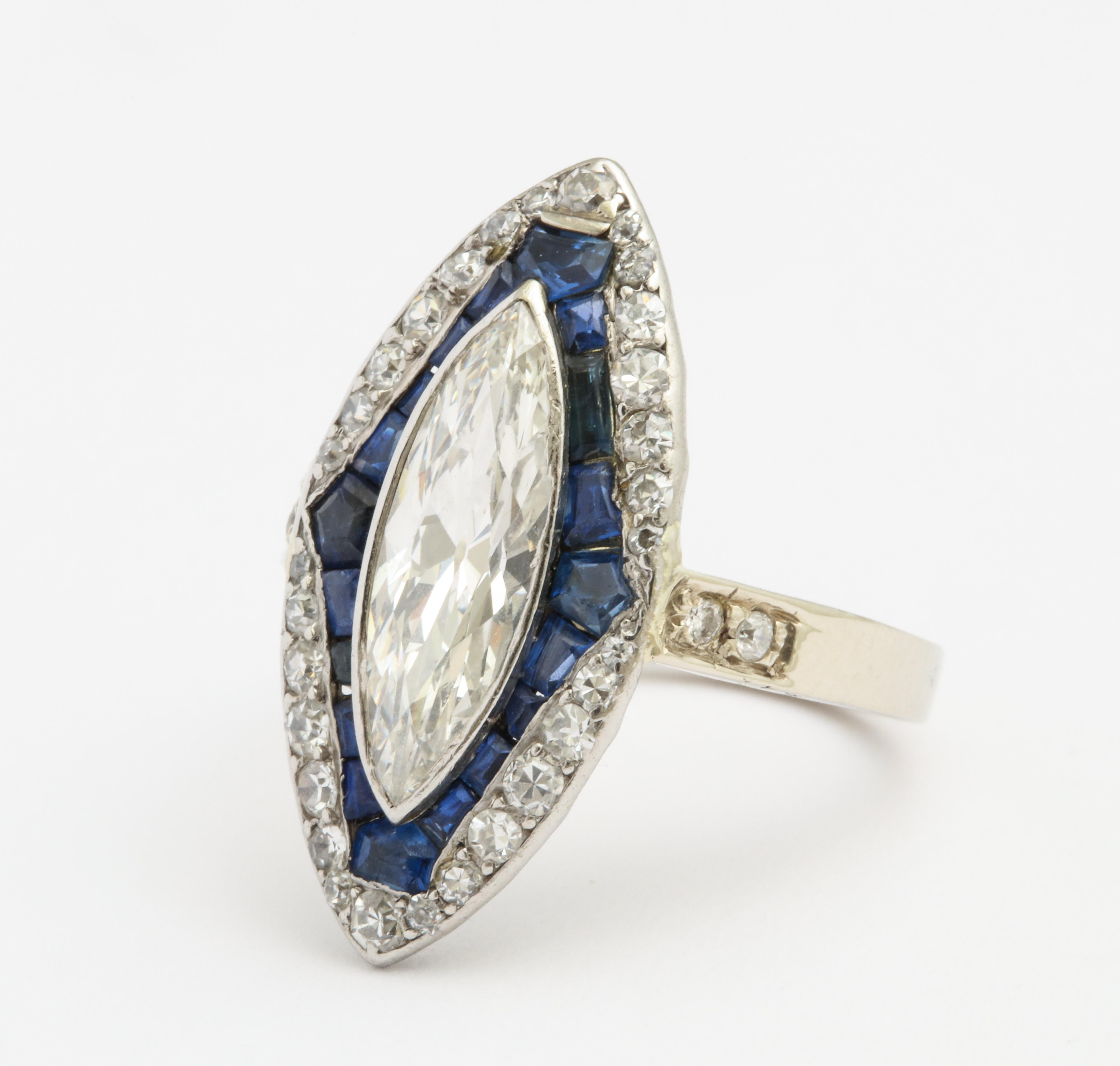 A Beautiful Art Deco period dinner ring, features a stunning high-color/clean (est G-H color VS1-2 clarity) marquise-cut diamond approx 1.85cts surrounded by calibre-cut bright blue sapphires and small old cut diamonds in the frame. Gorgeous detail