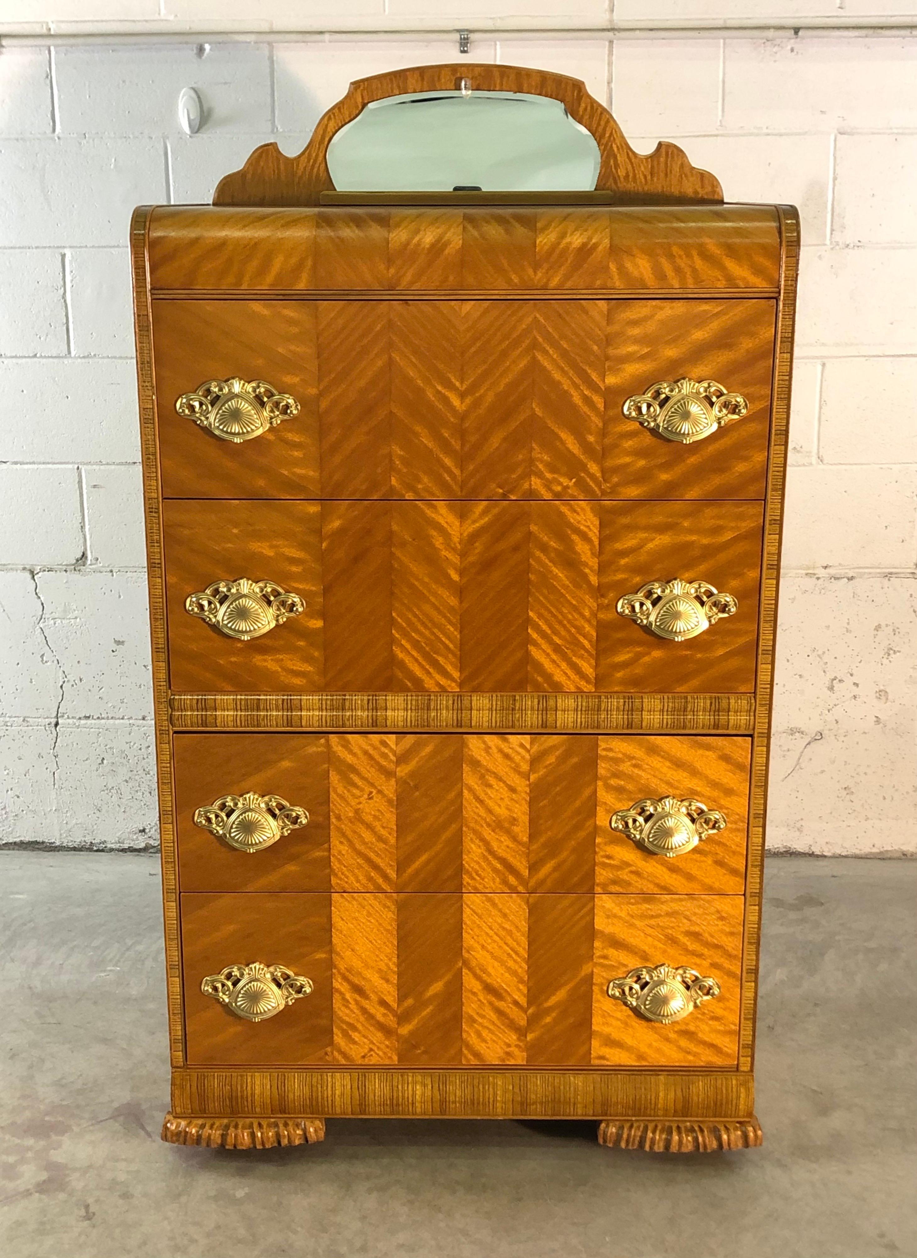 Art Deco tall waterfall-style highboy four drawer dresser with matchbook veneer and zebra wood accents. The dresser has a small mirror on top. The drawers are all 9” high for ample storage. Newly refinished condition and on castors. No marks.