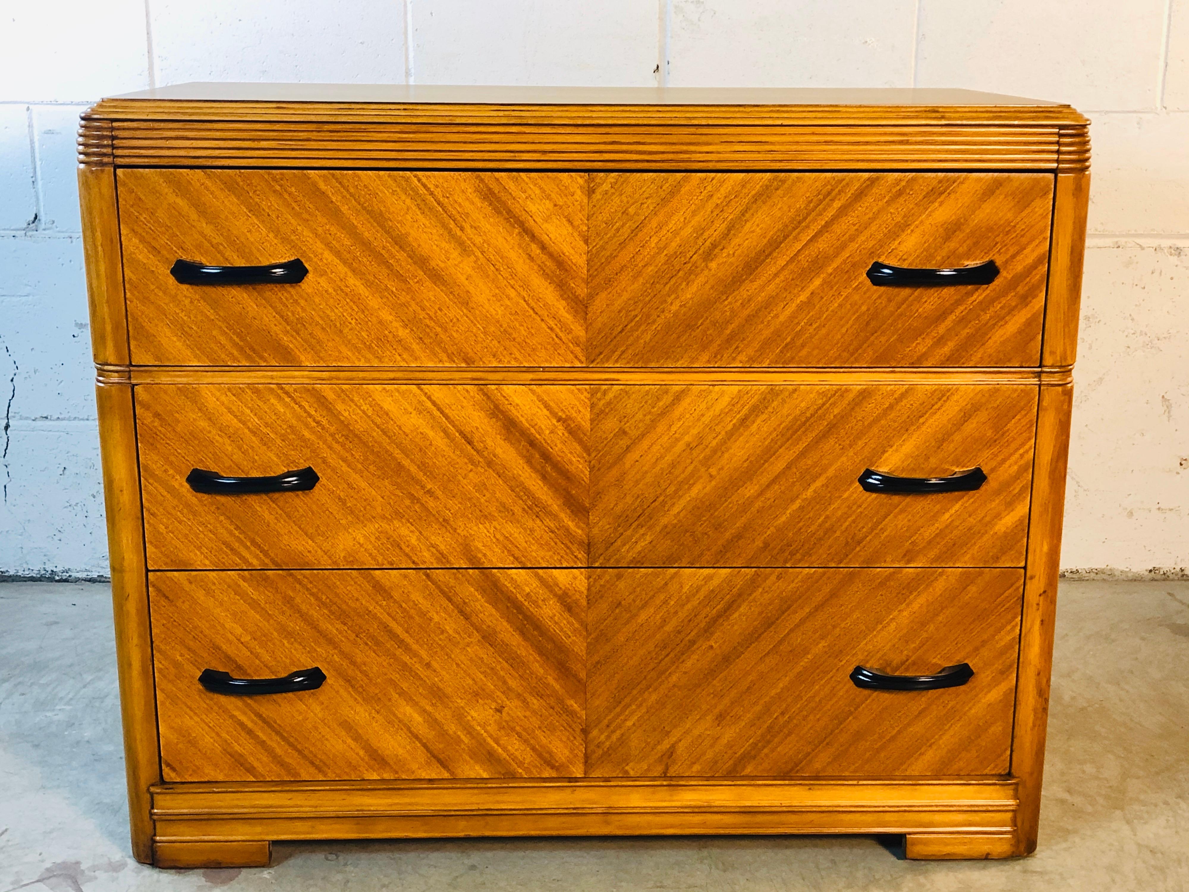 Art Deco matchbook veneer three drawer low dresser with black metal handles. The dresser has nice accents and is marked Huntley Furniture inside the drawer. The dresser is in refinished condition.