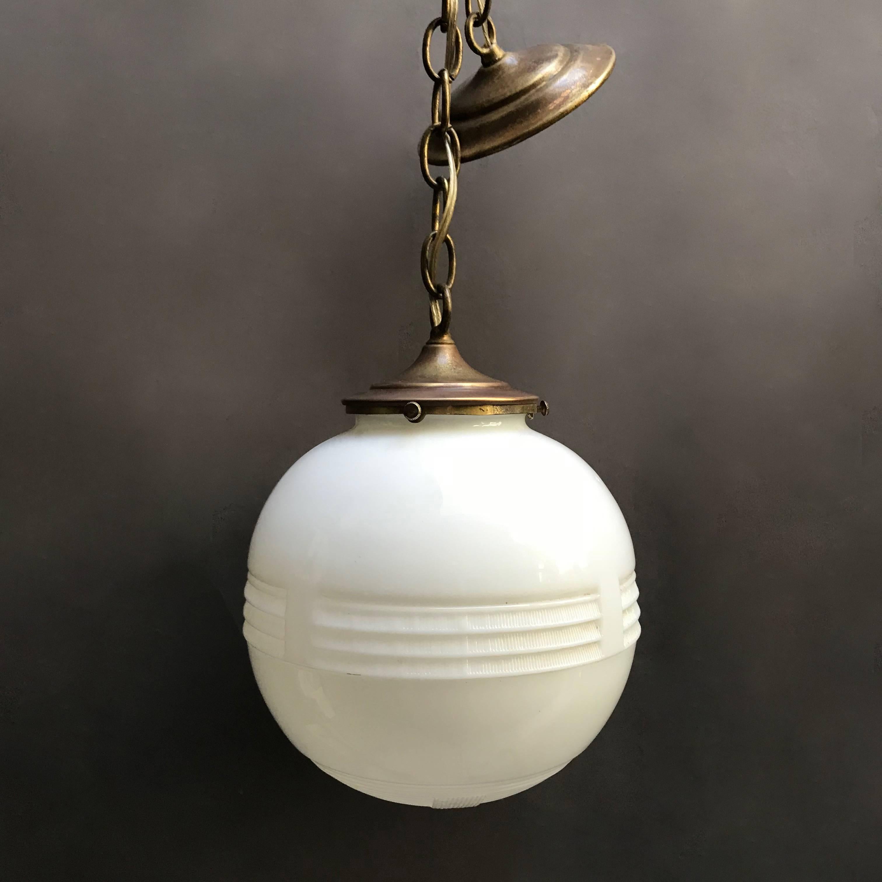 Art Deco pendant light features a decorative, milk glass globe shade with brass fitter, 26 inches of chain and canopy is newly wired to accept up to a 150 watt bulb. The chain height is adjustable but the full extent of the pendant is 36 inches.