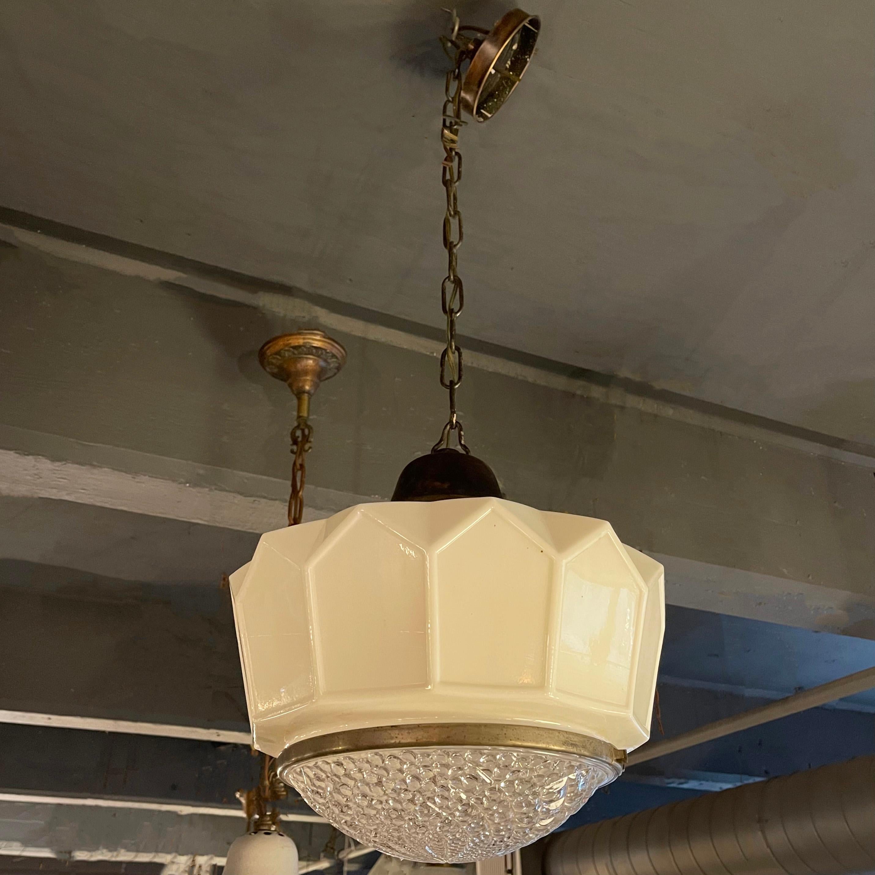 Art deco pendant light features a faceted milk glass shade with brass trimmed, textured clear glass diffuser on brass fitter, chain and canopy. The shade measures 13 inches ht and the overall height of the pendant is 38 inches but can be adjusted.