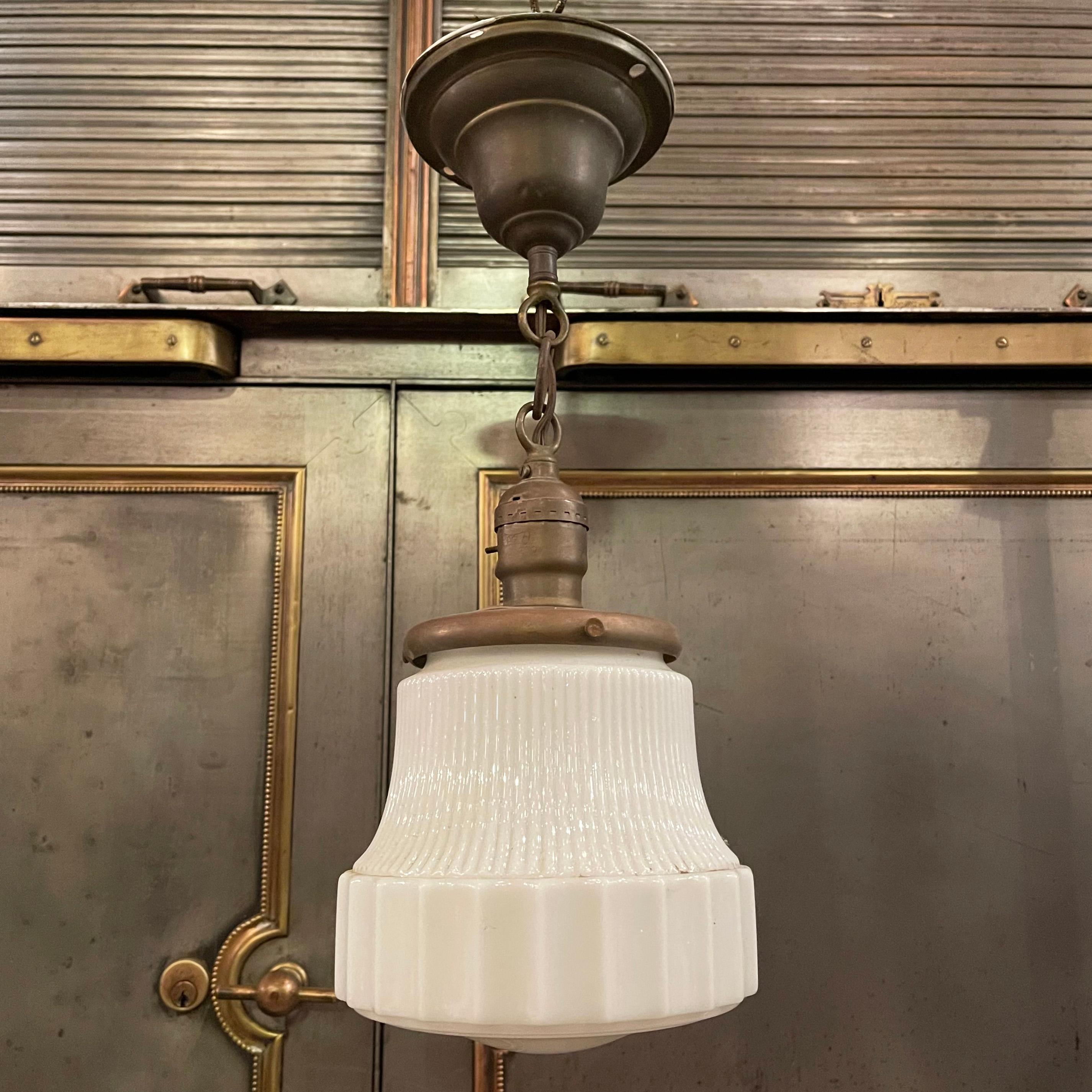 Art Deco pendant or semi-flushmount light with ribbed, milk glass shade on a brass fitter, chain and canopy. The pendant hangs at an overall height of 15 inches.