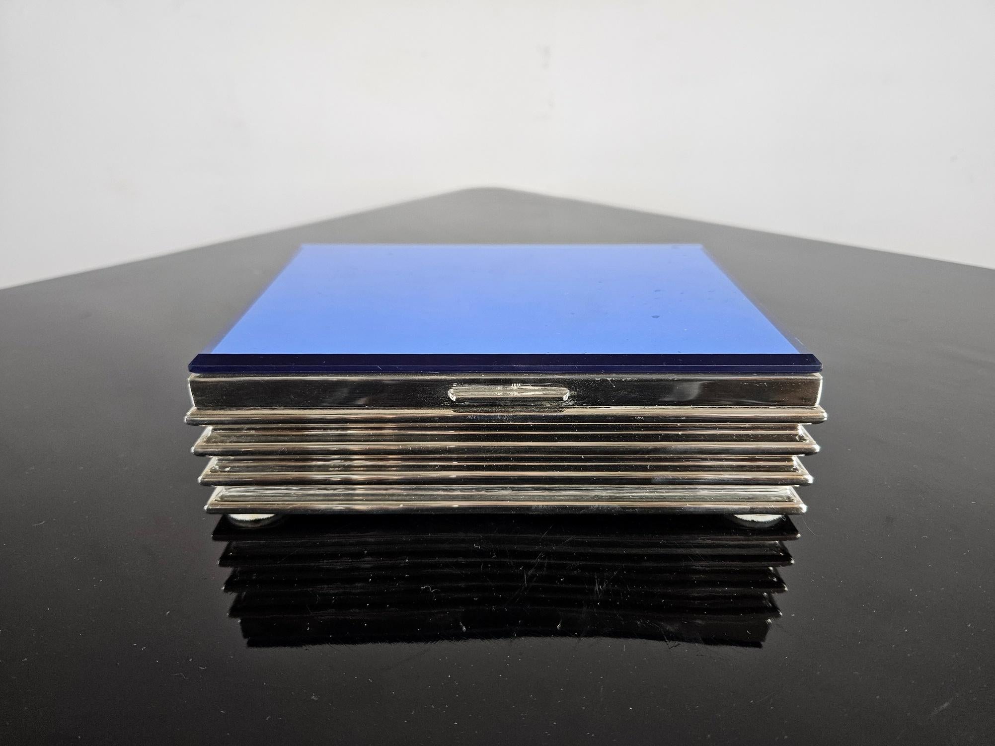 Joyero Art Déco de metal cromado y cristal azul de los años 30. Tiene un bonito y llamativo diseño en plata, azul y gris. El interior tiene un espejo en la tapa y espacio para varias joyas. Hay desgaste en el interior, que podría restaurarse, por