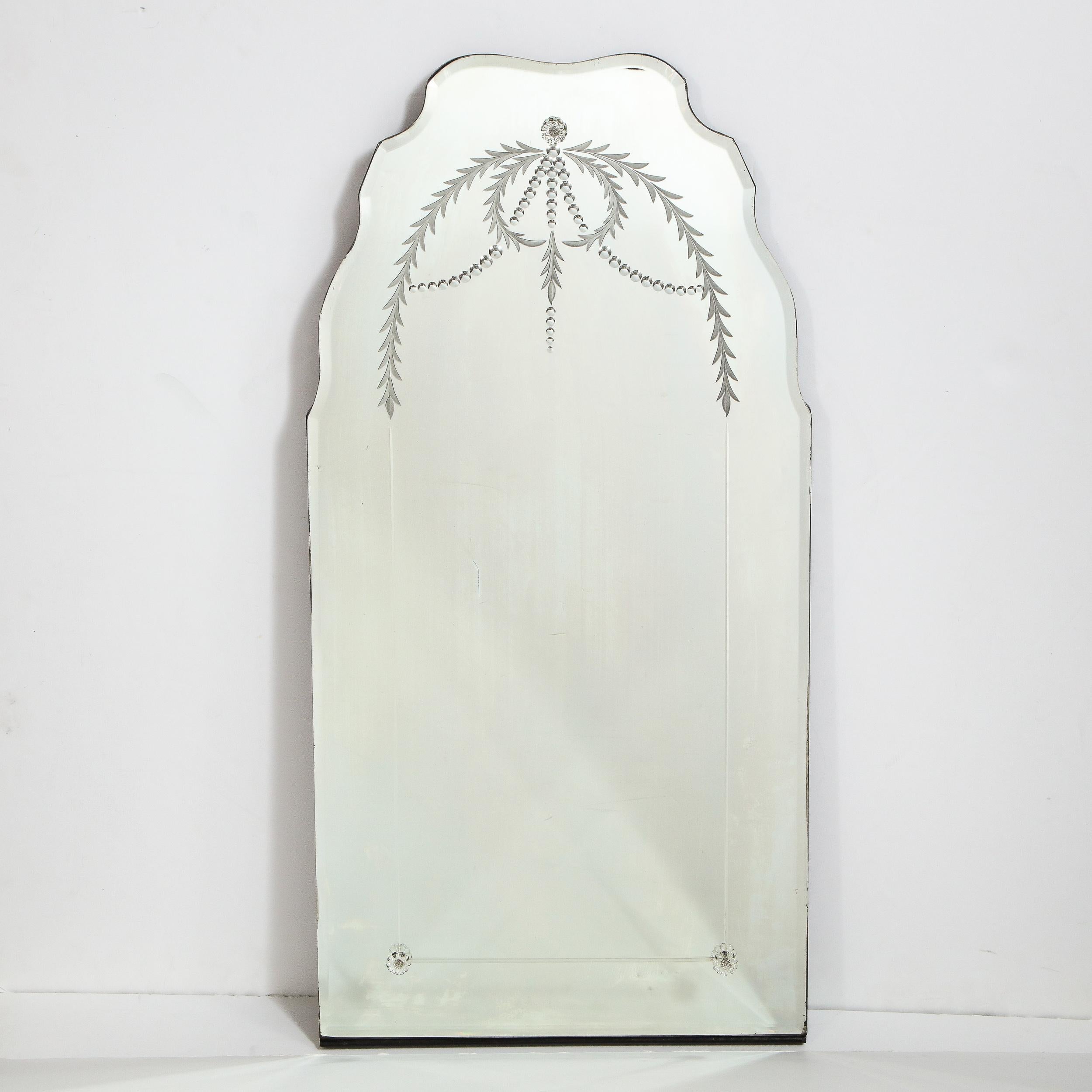This elegant Art Deco mirror was realized in the United States circa 1940. It features a scalloped beveled border wrapped in ebonized walnut with chain beveled circular and laurel wreath motifs etched into the glass. The center of the piece also has