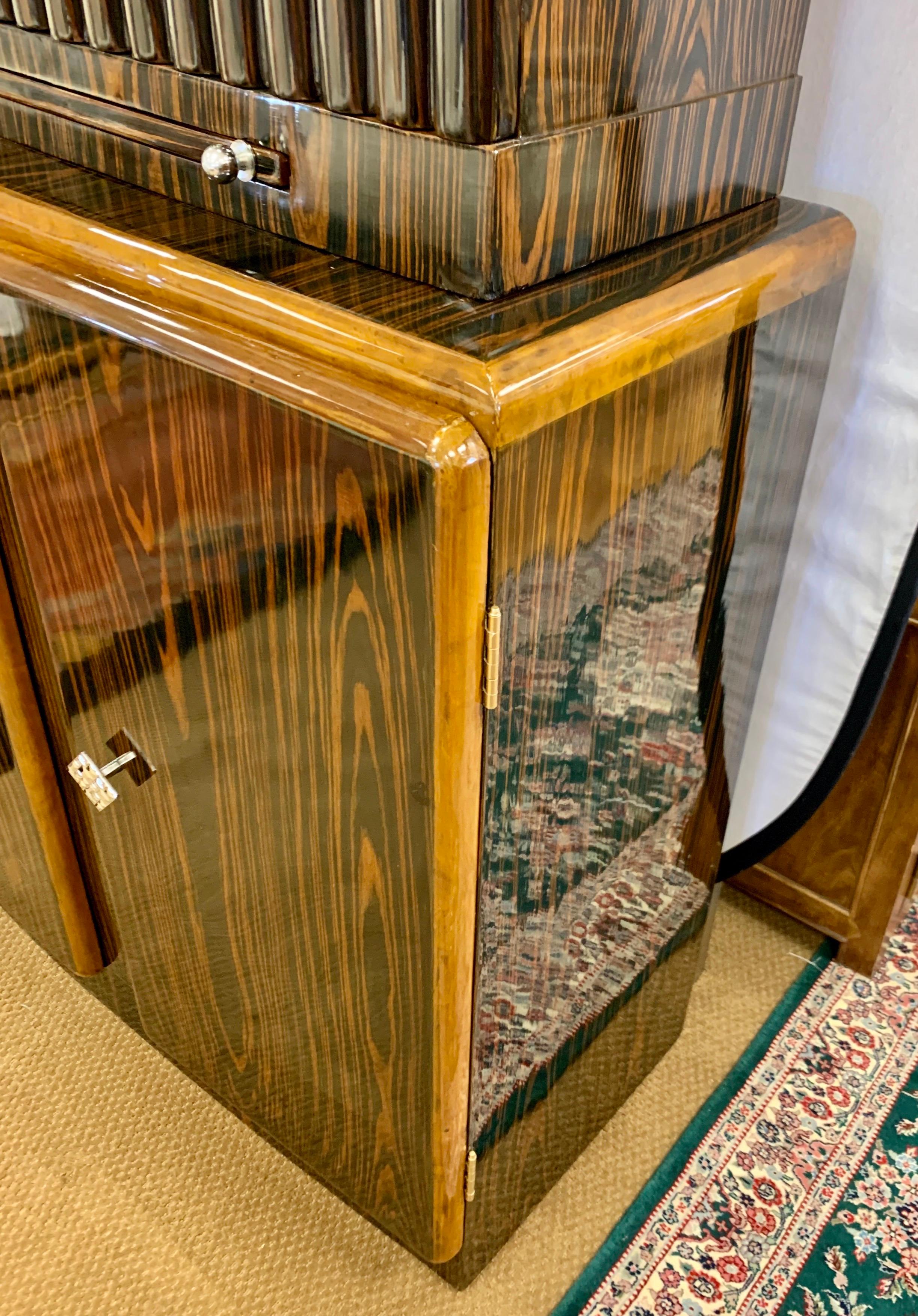 Swank and coveted Art Deco style bar where top has mirrored interior and bottom has ample storage.
See pics. Features Macassar wood and unusual metal hardware. Imported from Italy in the mid-20th century. Also features mirrored tray that pulls out