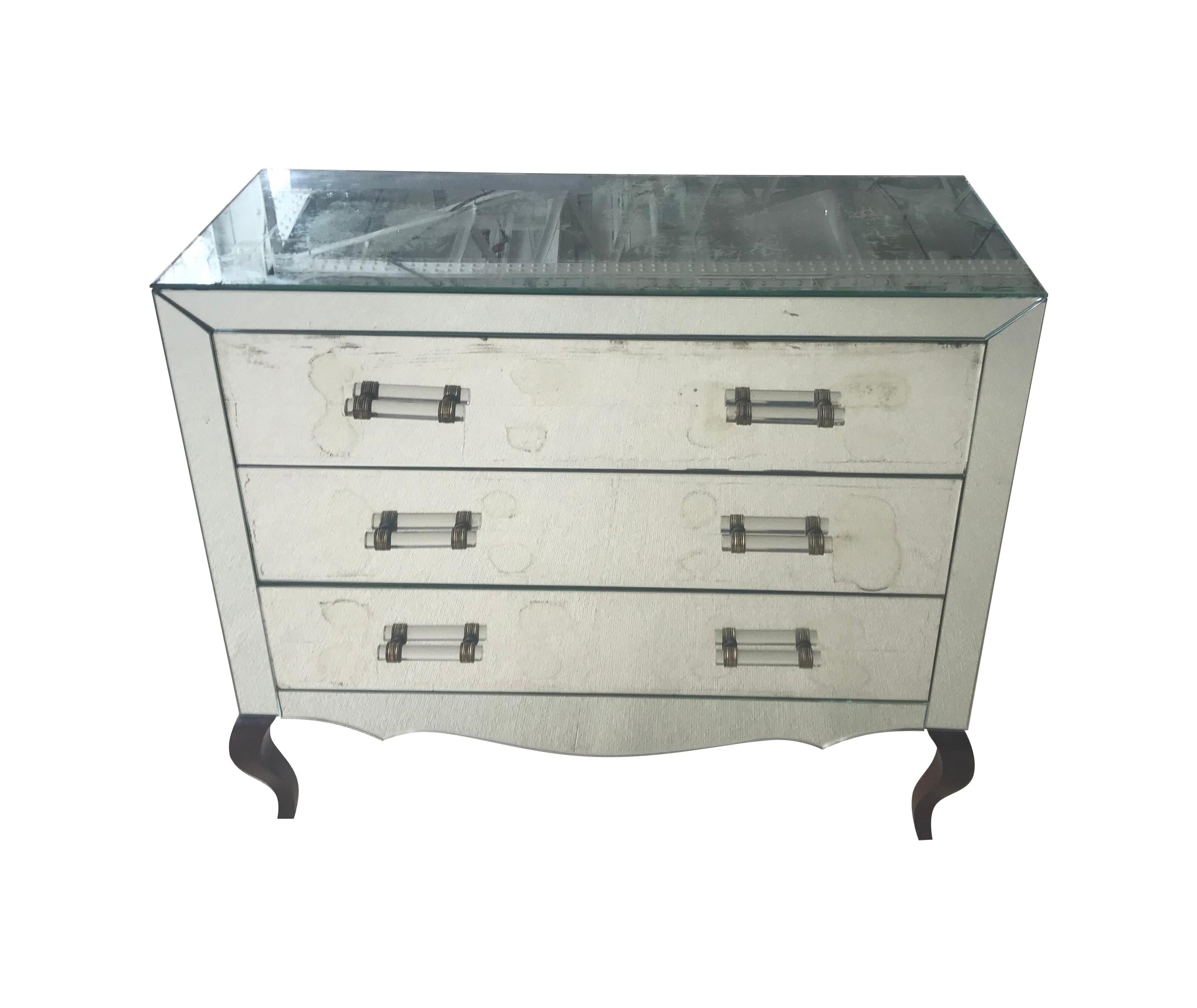 An Art Deco mirrored chest of drawers with three drawers each with two glass handles with brass detailing on. The interiors of the drawers are pine with ebonized saber feet. There is some original foxing on the mirror top and front, but part of the