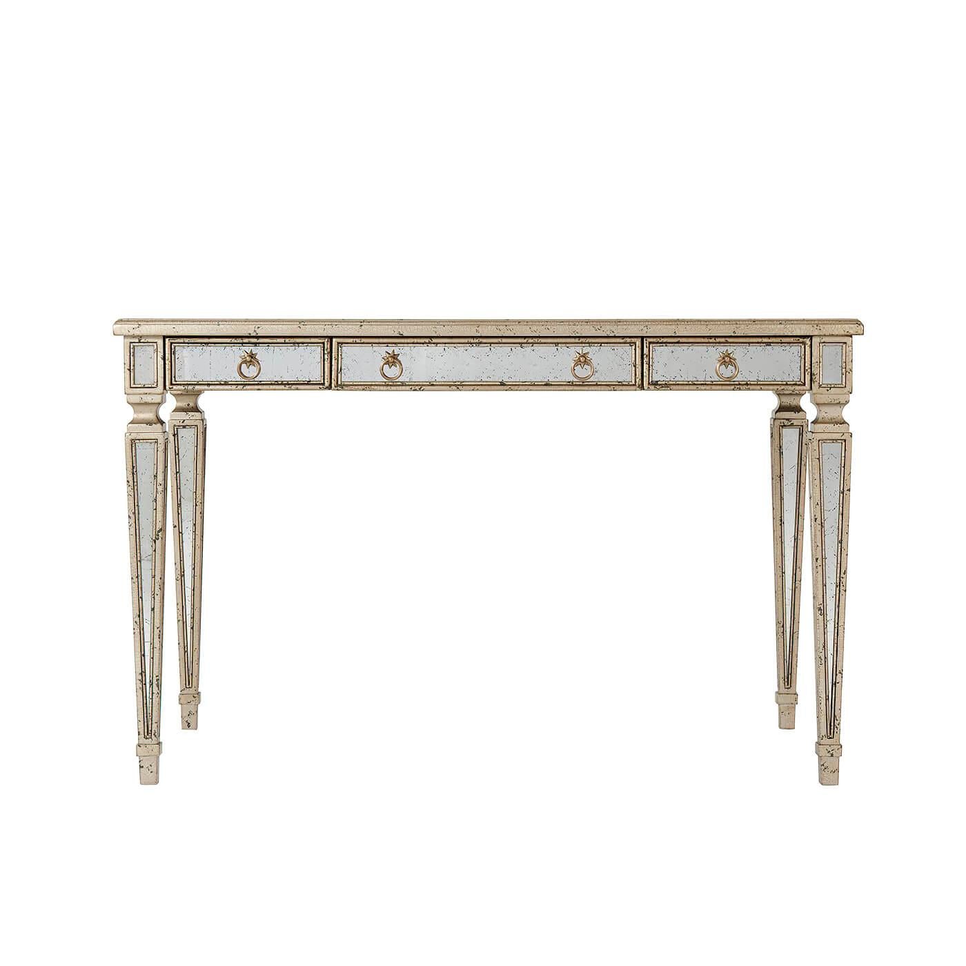 An Art Deco-style mirrored desk with silver leaf and antiqued mirror, the rectangular mirror paneled top above three drawers with brass handles, on mirror inset square tapering legs. Inspired by a 1930s Italian original.

Dimensions: 48