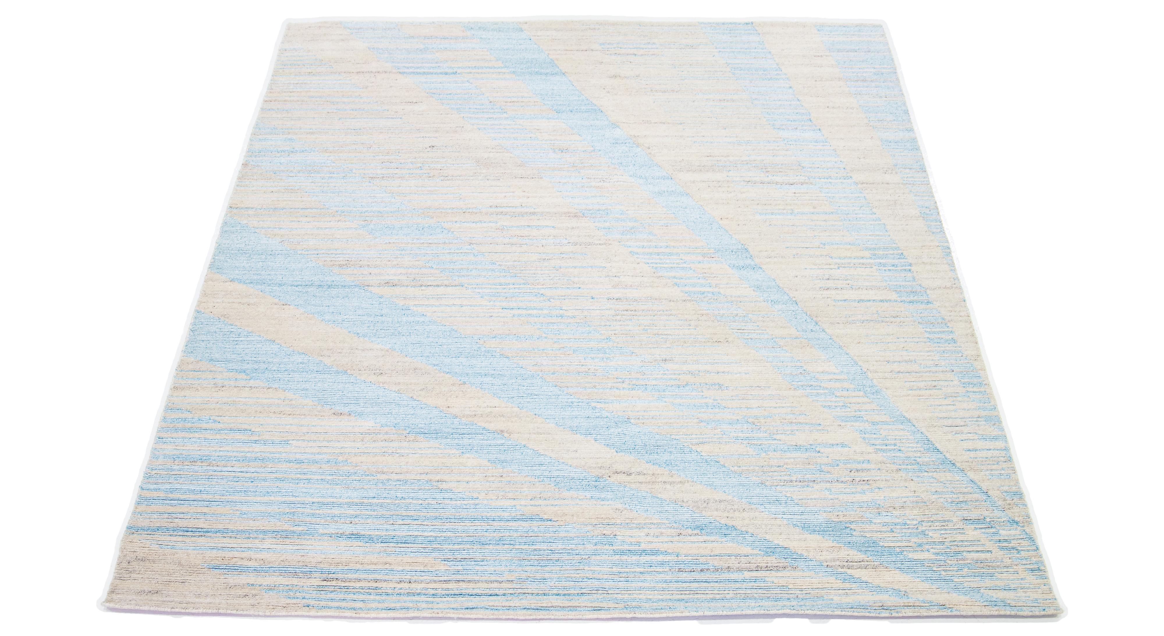 The contemporary art deco wool rug features a captivating abstract beige backdrop with elegant blue embellishments. The exquisitely crafted all-over pattern exudes the essence of modernism, epitomizing its significance in the 21st century.

This rug