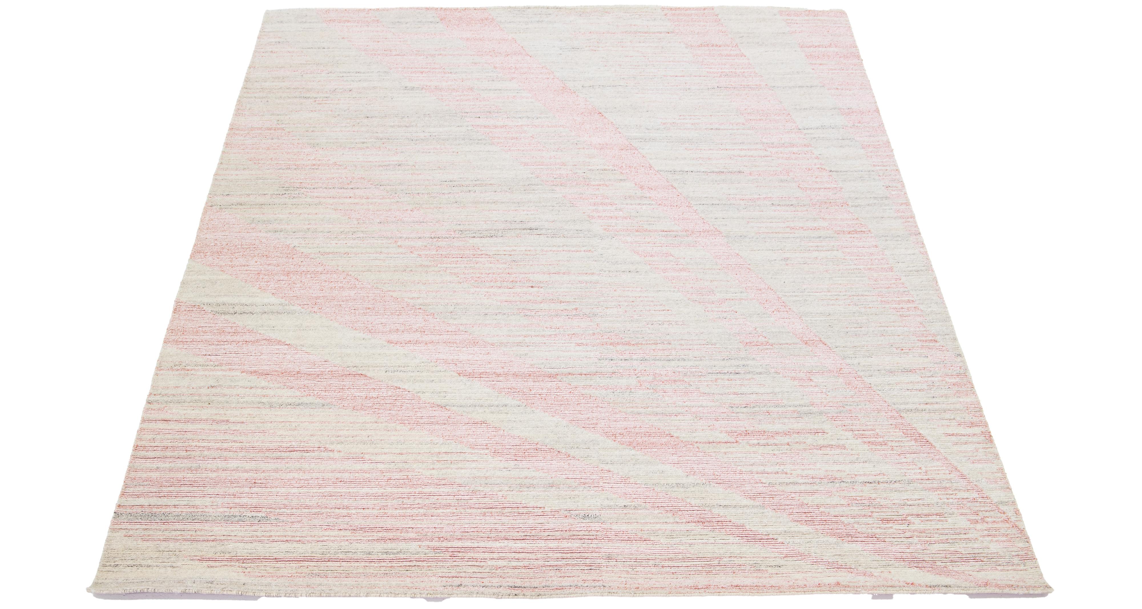 The contemporary art deco wool rug features a captivating abstract beige backdrop with elegant pink embellishments. The exquisitely crafted all-over pattern exudes the essence of modernism, epitomizing its significance in the 21st century.

This rug