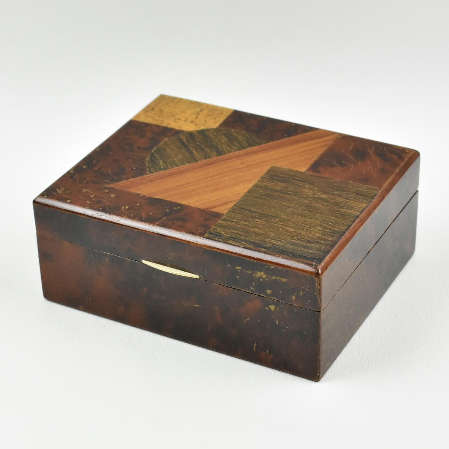 Elegant Art Deco decorative lidded box, featuring a square minimalist shape with varnished burl wood and tiny bone handle. Lid is decorated with different quality wood marquetry in geometric design. Interior in mahogany. No visible
