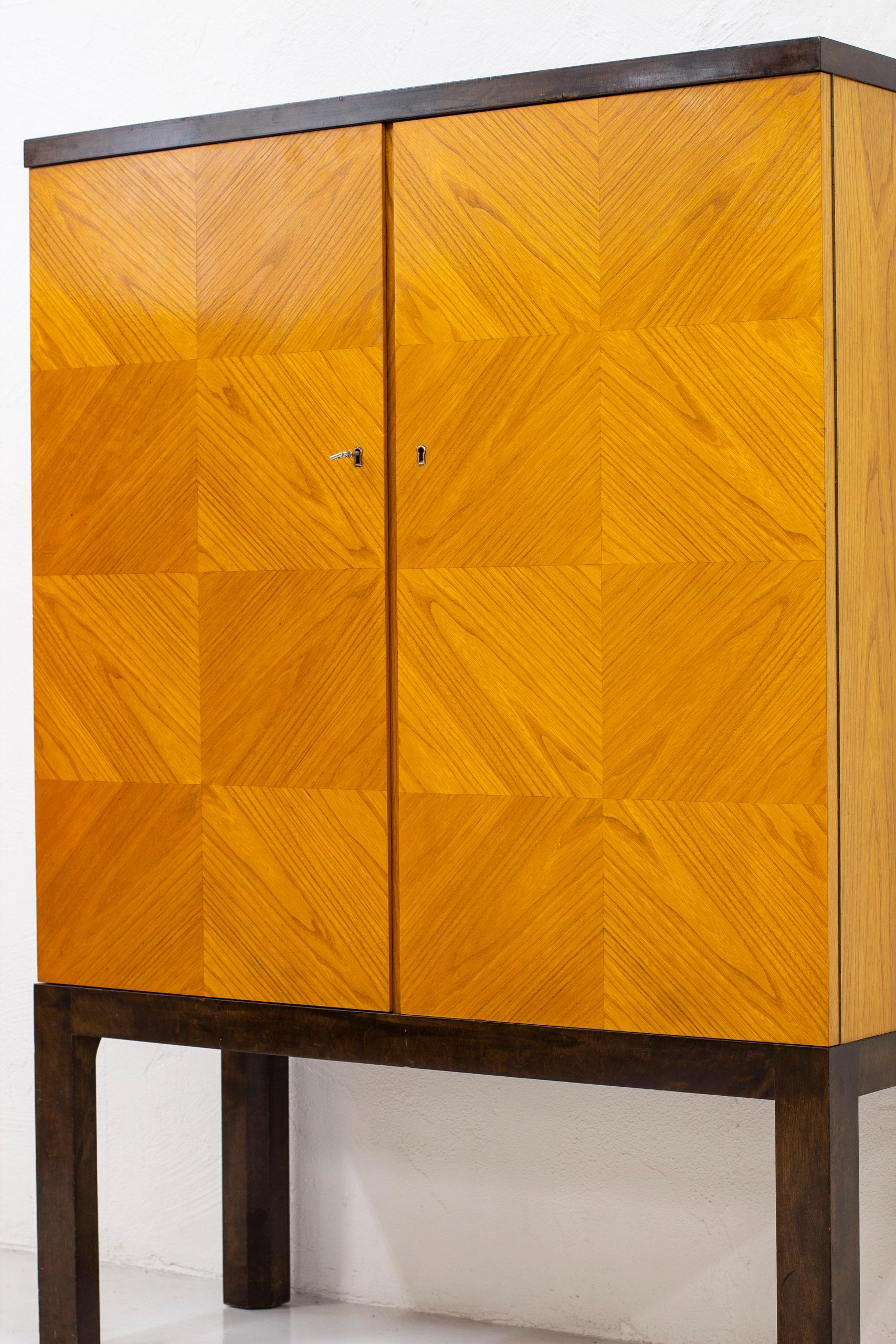 Modernist/Art Deco cabinet in the style of Otto Schulz. Produced in Sweden by unknown cabinetmaker during the 1930s. Stained birch legs and top with doors veneered in a checker board pattern in elm wood. Inside of the cabinet veneered in oak with