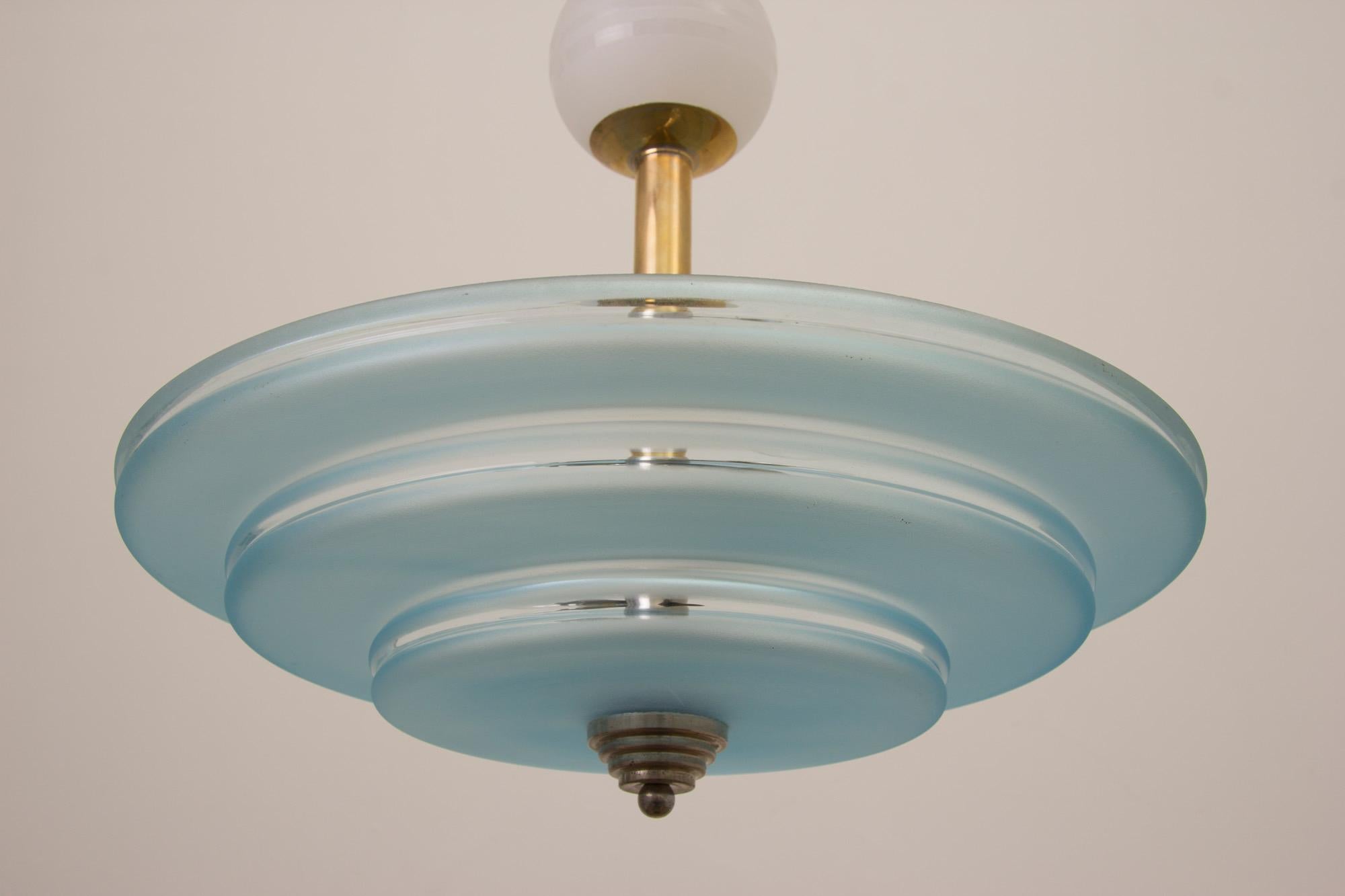 Art Deco modernist Bauhaus ceiling pendant.
Very impressive Art Deco ceiling light with stepped pale blue glass shade suspended on a two-tone polished brass and nickel plate column with white ceramic ball.
Measures: H 58 cm, W 41 cm, D 41