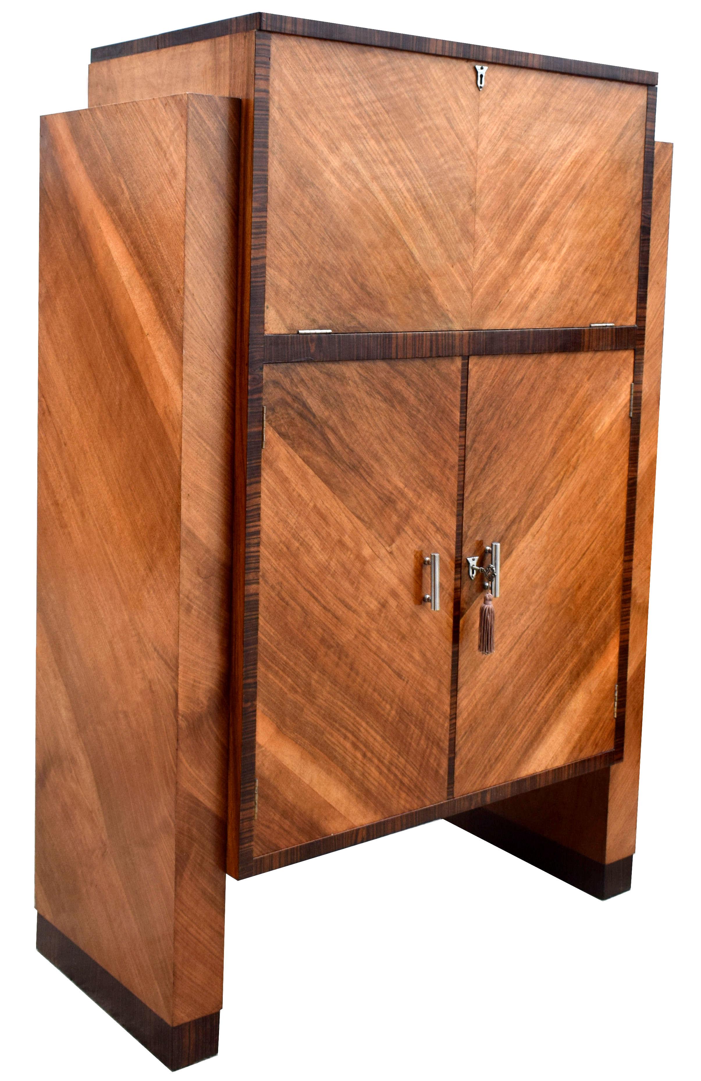 An original Art Deco modernist cocktail cabinet, dry bar in walnut & Macassar ebony, circa 1930 originating from England. Every Deco interior should have one of these! Features a drop down top which reveals a mirrored interior which acts as storage