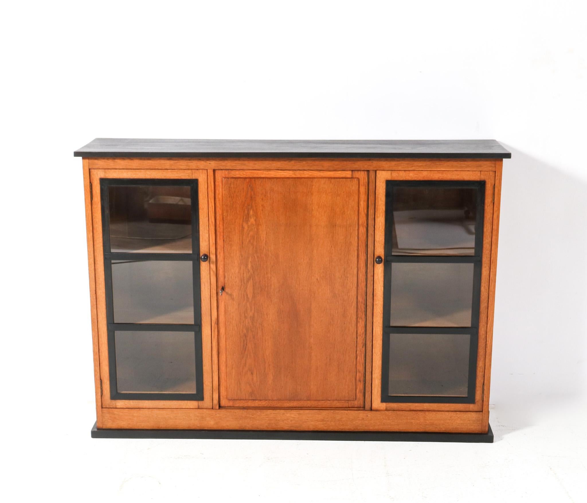 Magnificent and rare Art Deco Modernist bookcase.
Design by Jan Brunott.
Striking Dutch design from the 1920s.
Solid oak base with original black lacquered elements and original ebony handles on the doors.
Original black lacquered top.
Locks and