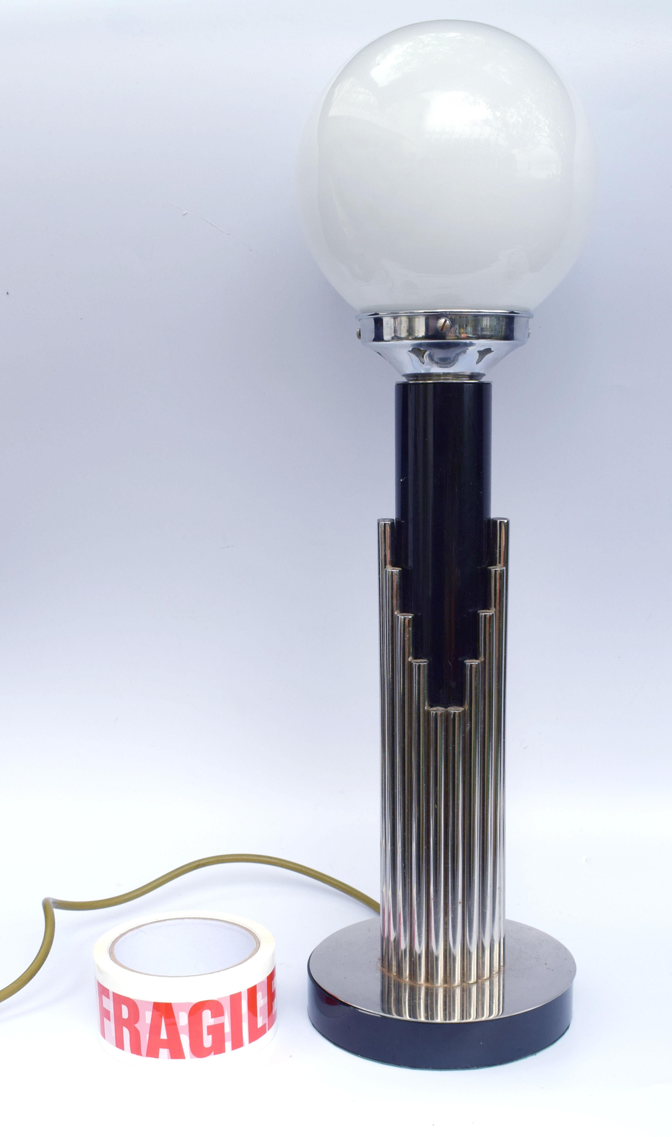 Offered for your consideration is this very tall English Art Deco style modernist table lamp. The chrome rods which surround the central ebonized column offer the look of a skyscraper skyline at night. A chrome gallery and milk white glass globe