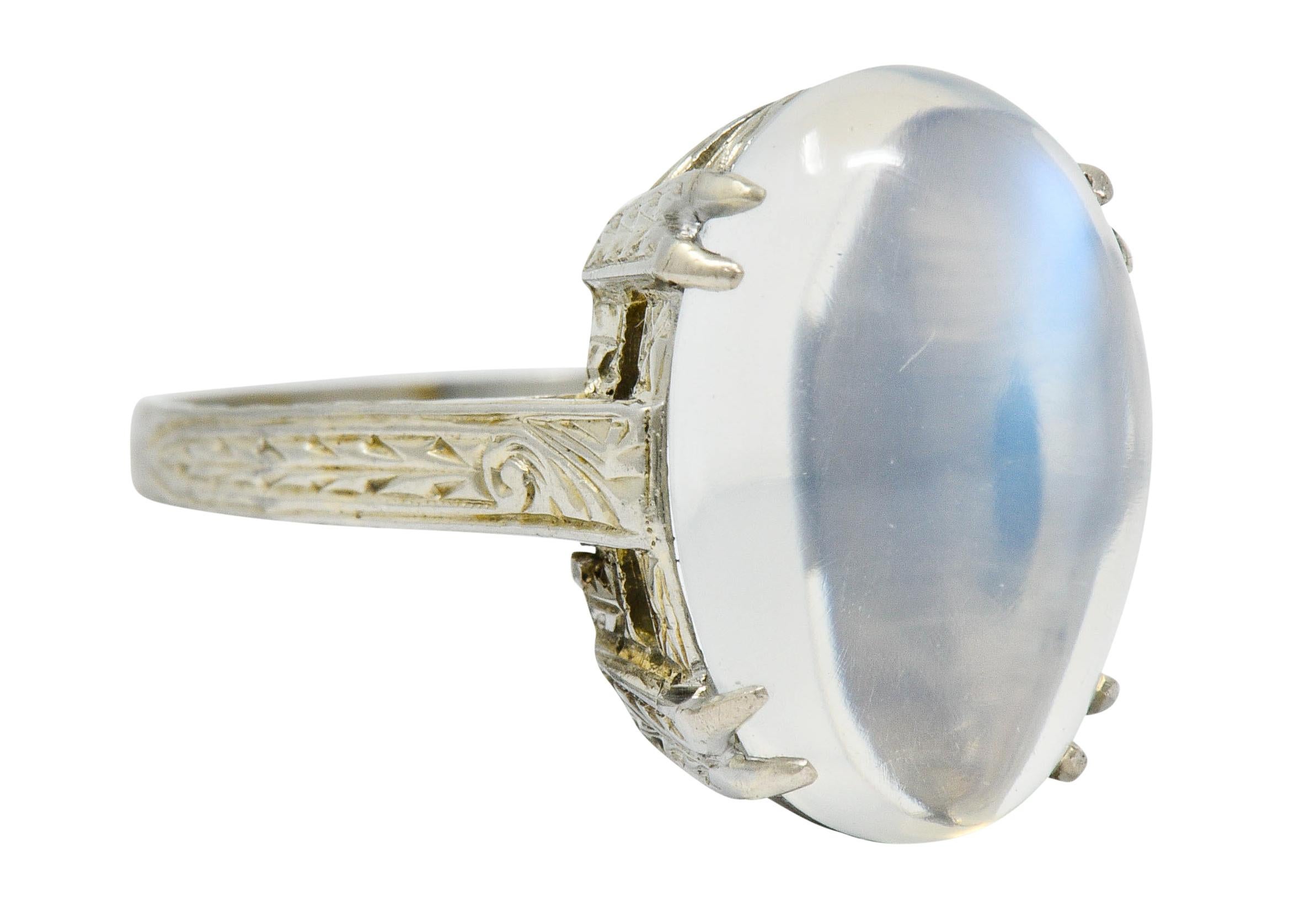 Centering an oval moonstone cabochon measuring approximately 15.5 x 10.4 mm

Translucent with moderately strong bluish-white adularescence

Basket set with stylized split prongs and emphasized by slight cathedral shoulders

Deeply hand engraved
