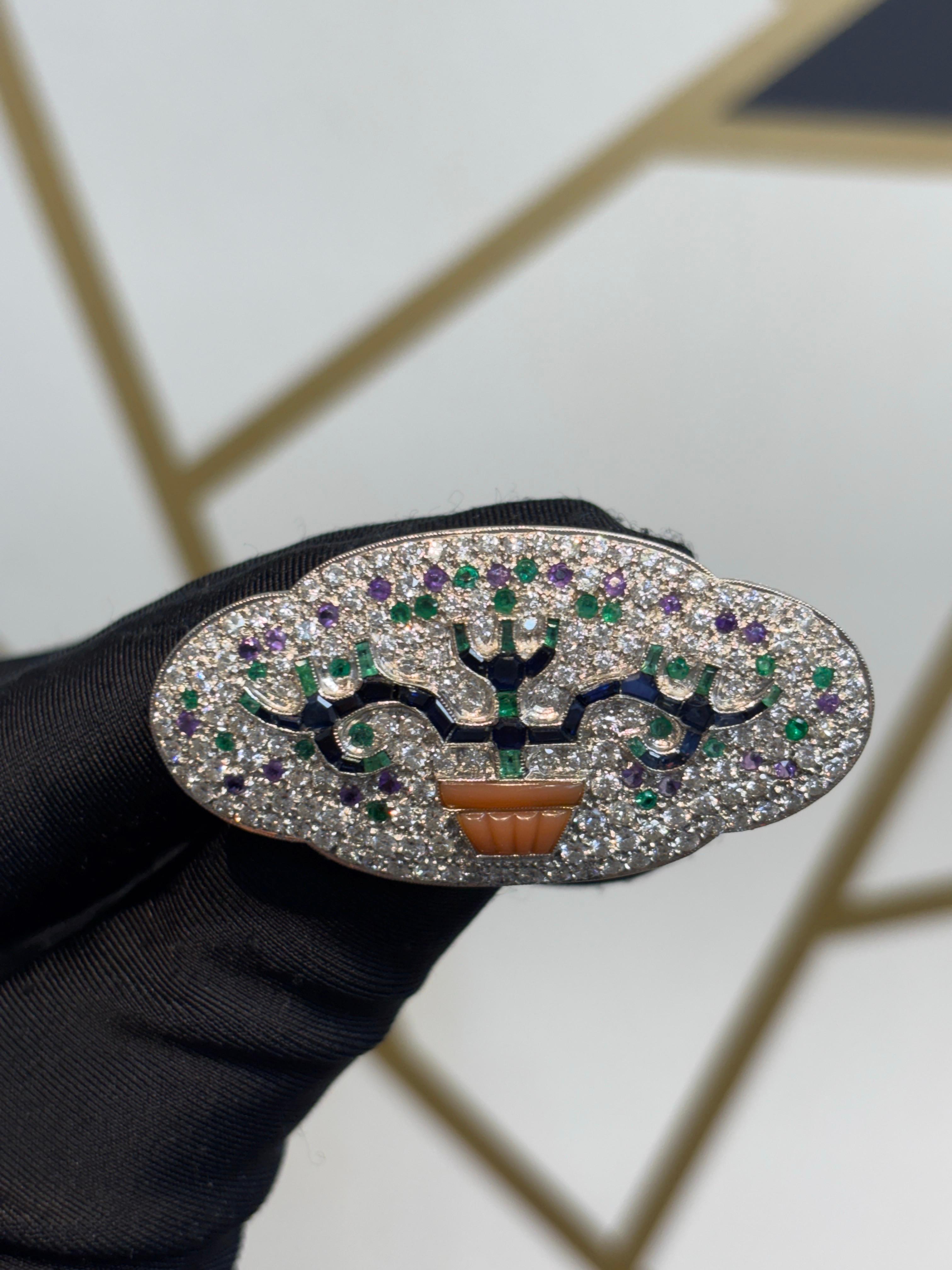 Broche Giardinetto Art déco à pierres précieuses multiples 

Broche à motif de giardinetto présentant des branches de saphir et d'émeraude, serties dans un pot de corail. Le fond est pavé de diamants avec des pierres d'améthyste et d'émeraude