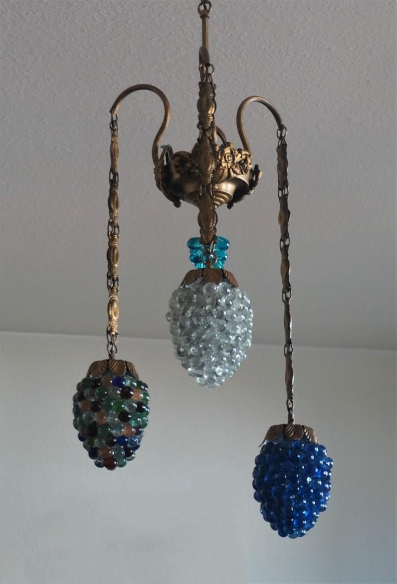 Murano glass three-light chandelier with cast iron and brass mounts, Italy, mid-20th century. Three brass hanging chains with colored and clear glass bunch of grapes form shades connected to a circular canopy decorated with three cast iron flower