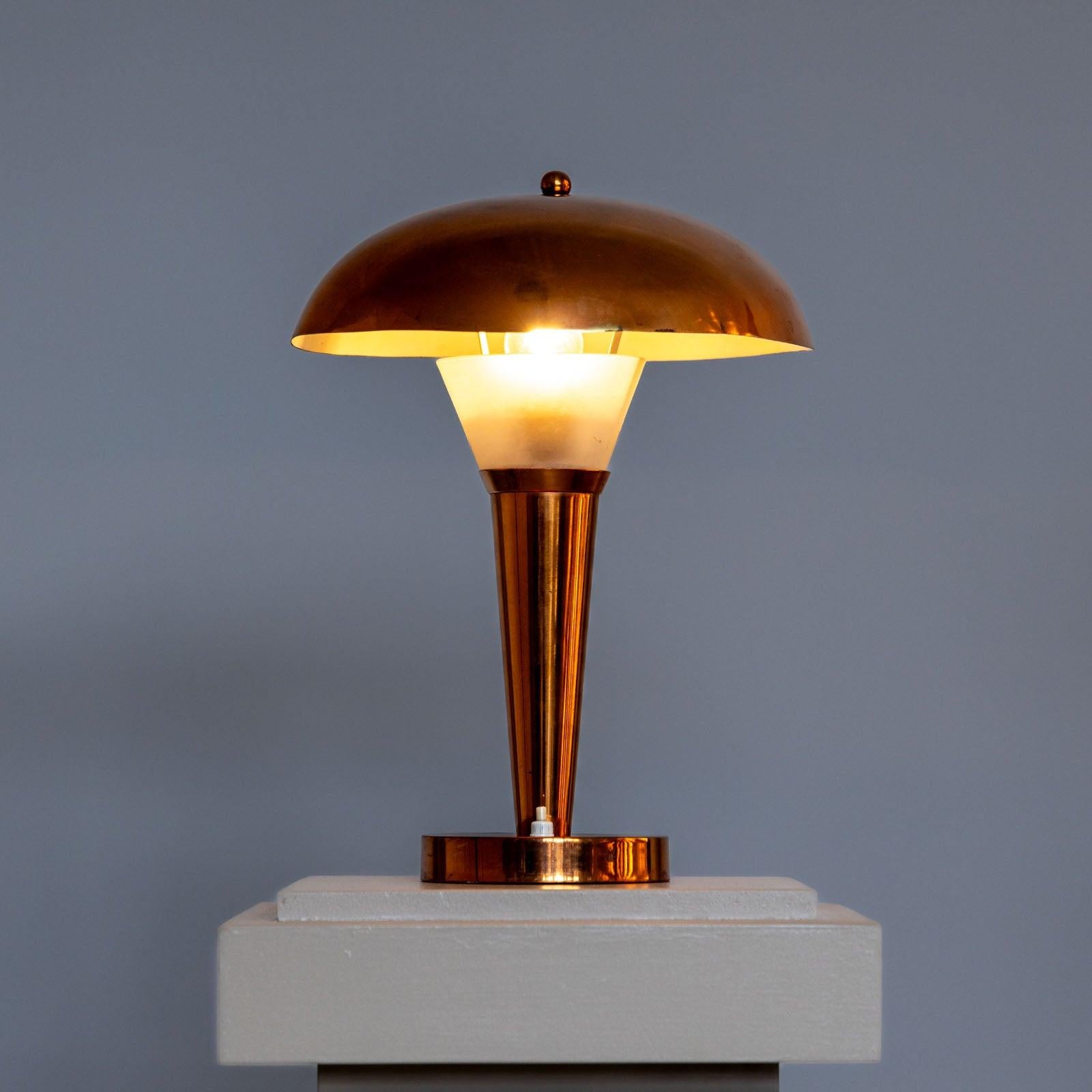 Lampe de table Art Déco en cuivre avec abat-jour en forme de champignon et base en forme d'entonnoir. L'extrémité supérieure de la base est en verre opaque. L'interrupteur est situé sur la base ronde. 