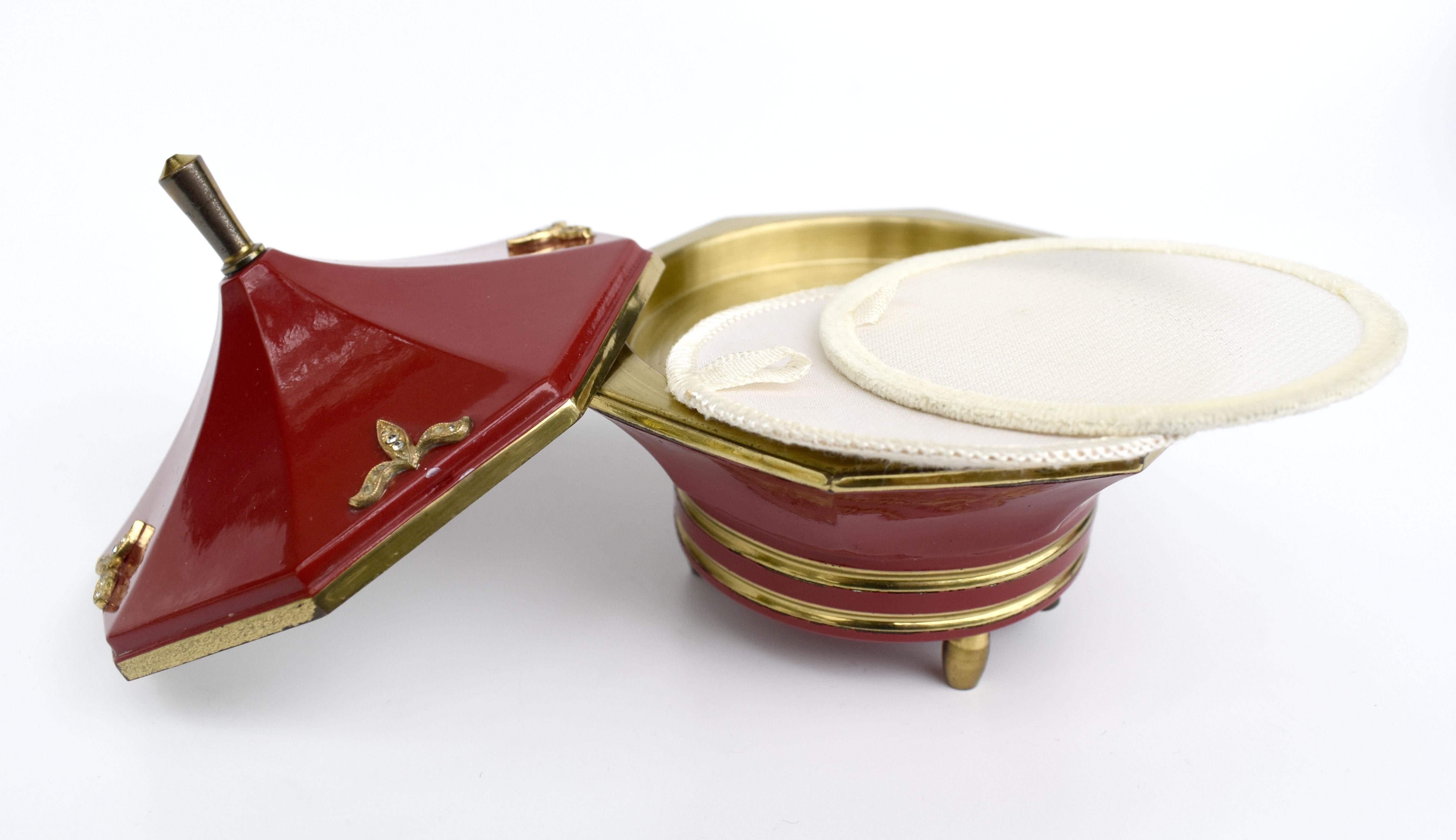 Beautiful Art Deco ladies musical powder box. It appears to not have ever been used and as such is in remarkable condition. Bright red enamel exterior with gold accents to the edges and feet. The interior is also brass and in mint unused condition.