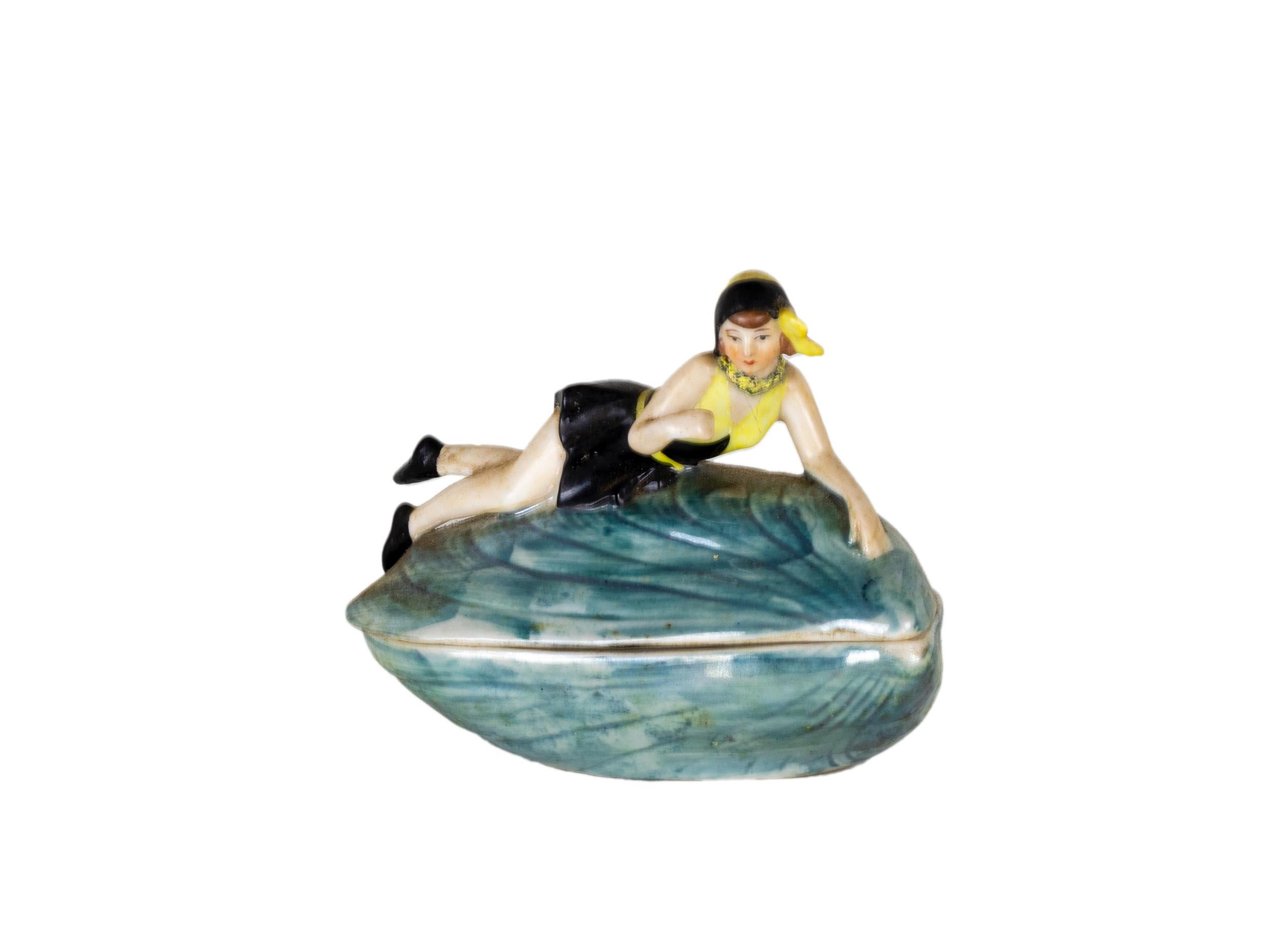 A nacre color Mussel Shell Rice Powder Box figurine in porcelain of a bathing lady in shell / Pin Up girl -style Baigneuse / Petite baigneuse.

10392 marked on the piece.
by W Goebel of Rodental Bavaria
