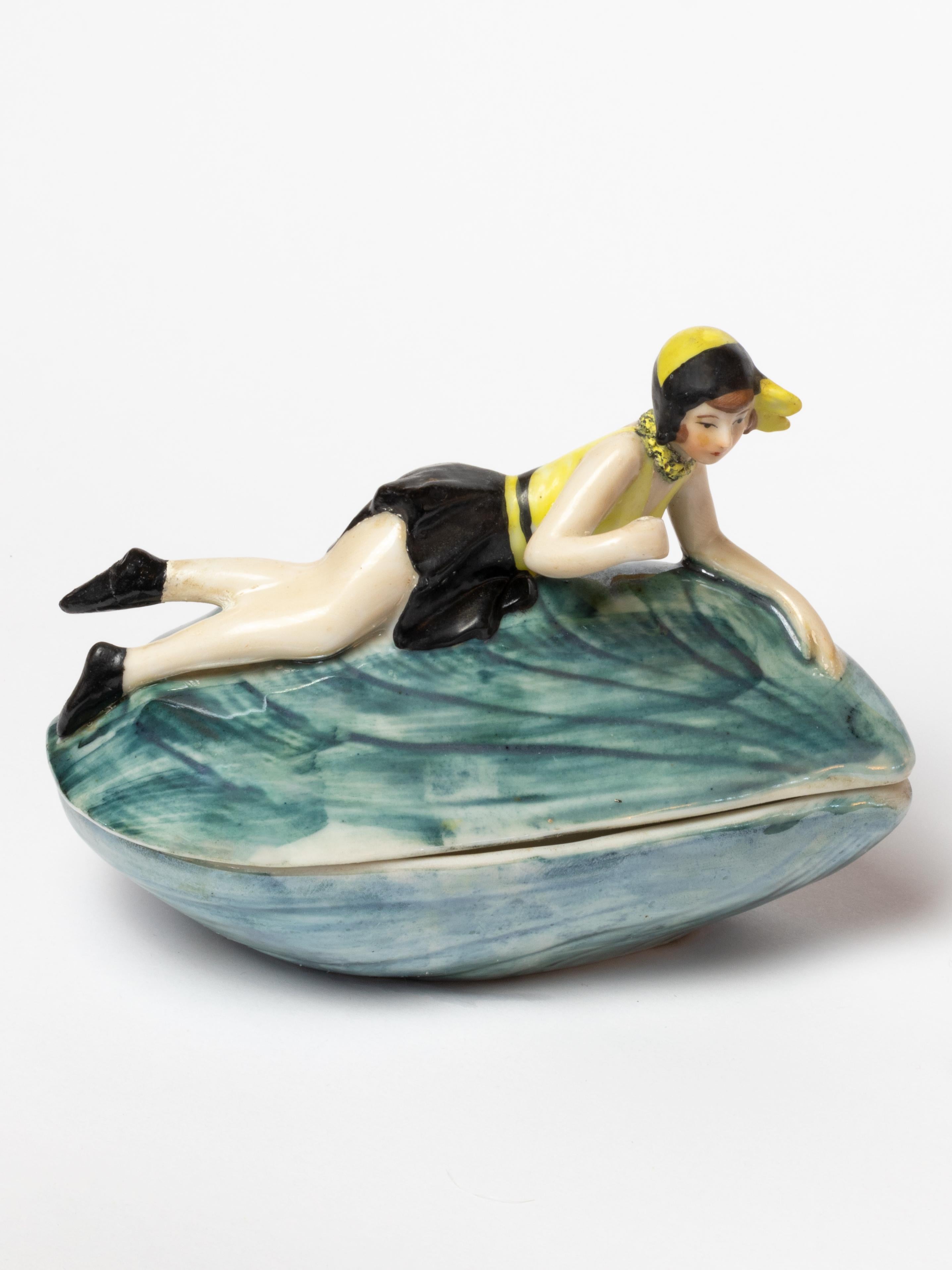 A nacre color Mussel Shell Rice Powder Box figurine in porcelain of a bathing lady in shell / Pin Up girl -style Baigneuse / Petite baigneuse.

10392 marked on the piece.
by W Goebel of Rodental Bavaria
