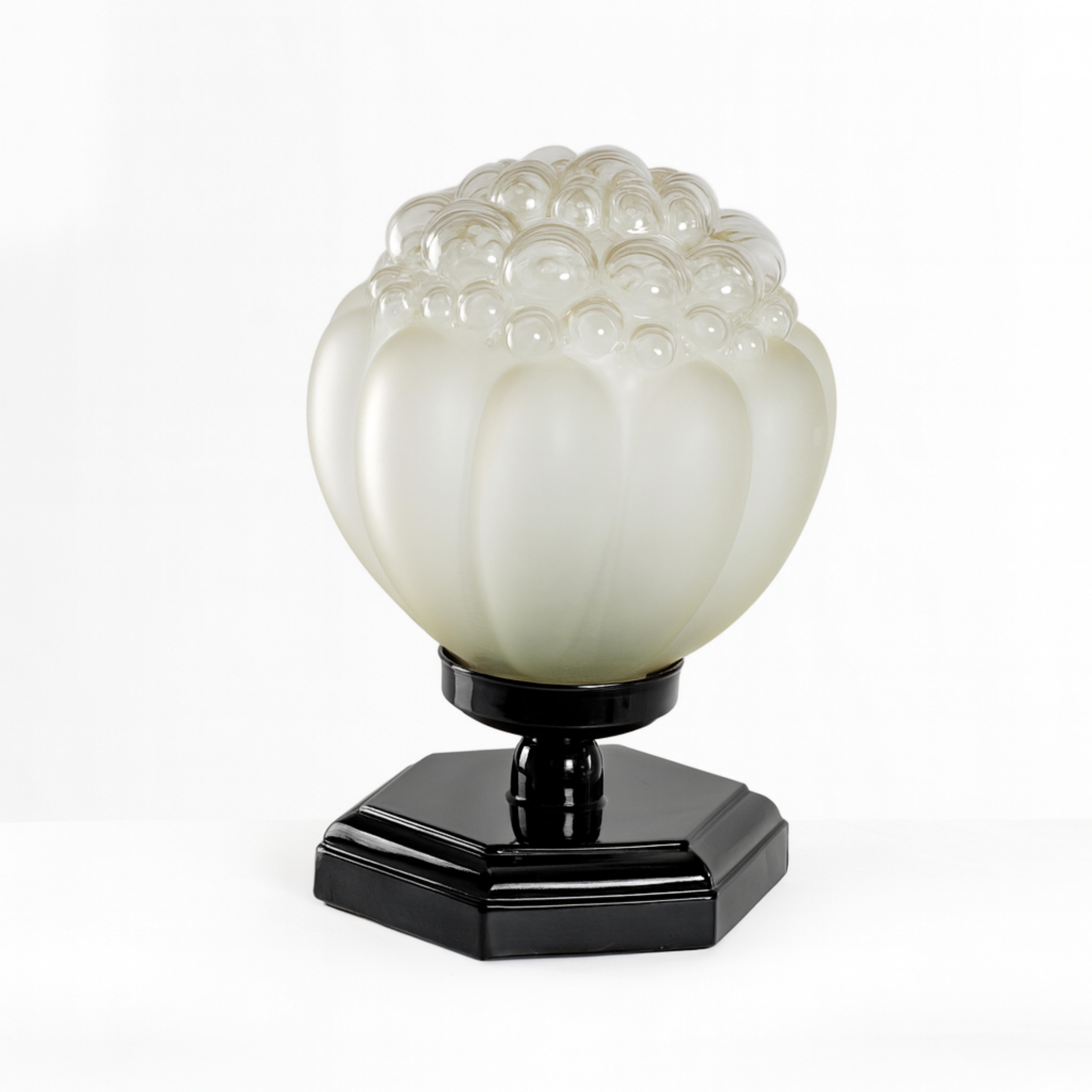 Élégante lampe de table Art déco en laque noire avec abat-jour en verre soufflé et base hexagonale en chrome poli.
L'abat-jour en verre soufflé a une finition nacrée qui capte doucement la lumière, créant une lueur chaude et sophistiquée.

Sa base