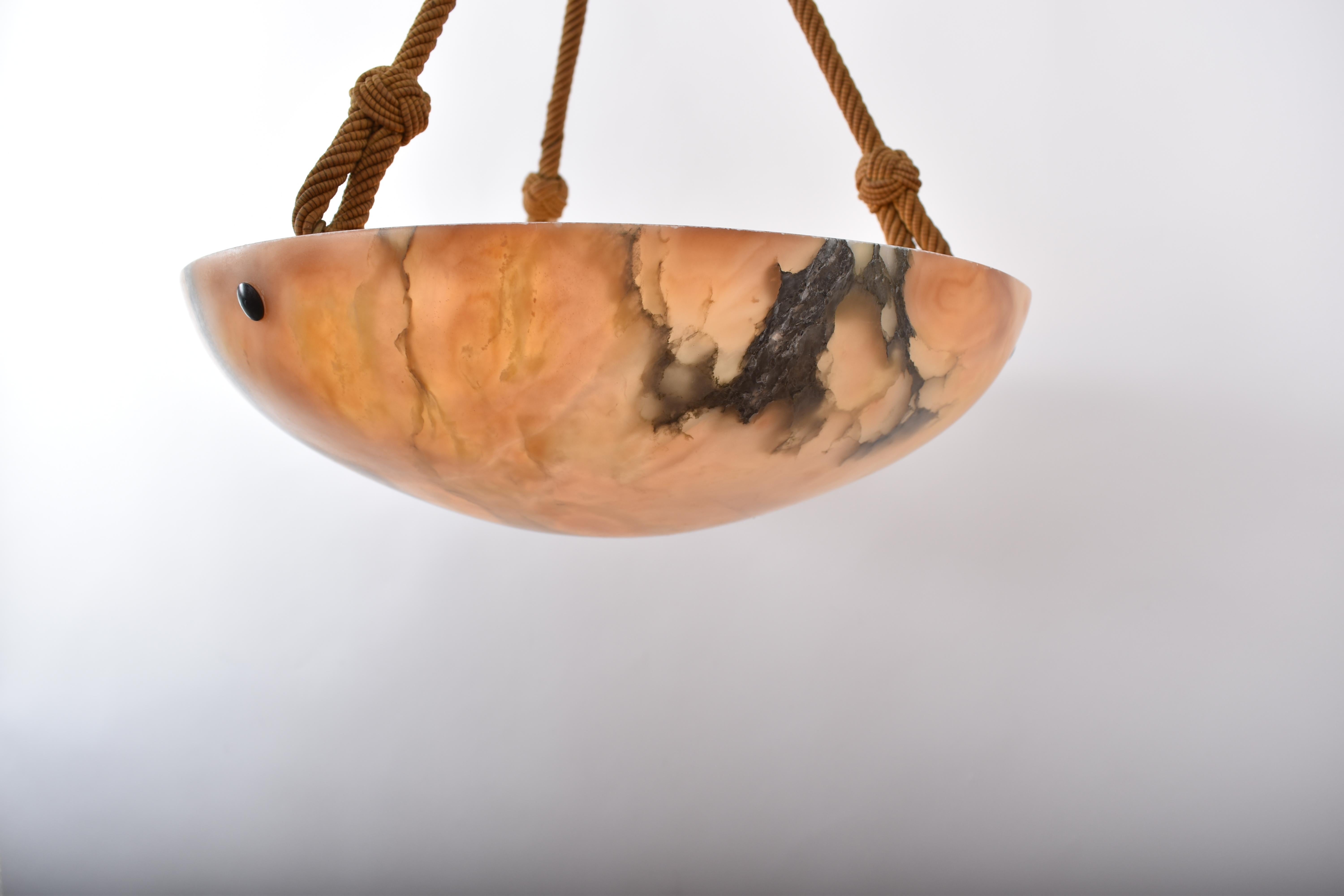 Natural art deco amber toned alabaster pendant lamp. 
It was  hand carved in Switzerland in the early decades of last century.
The lamp has an attractive amber to Sienna veining, giving a comfortable and soft lighting. 
Suspended on three ropes from