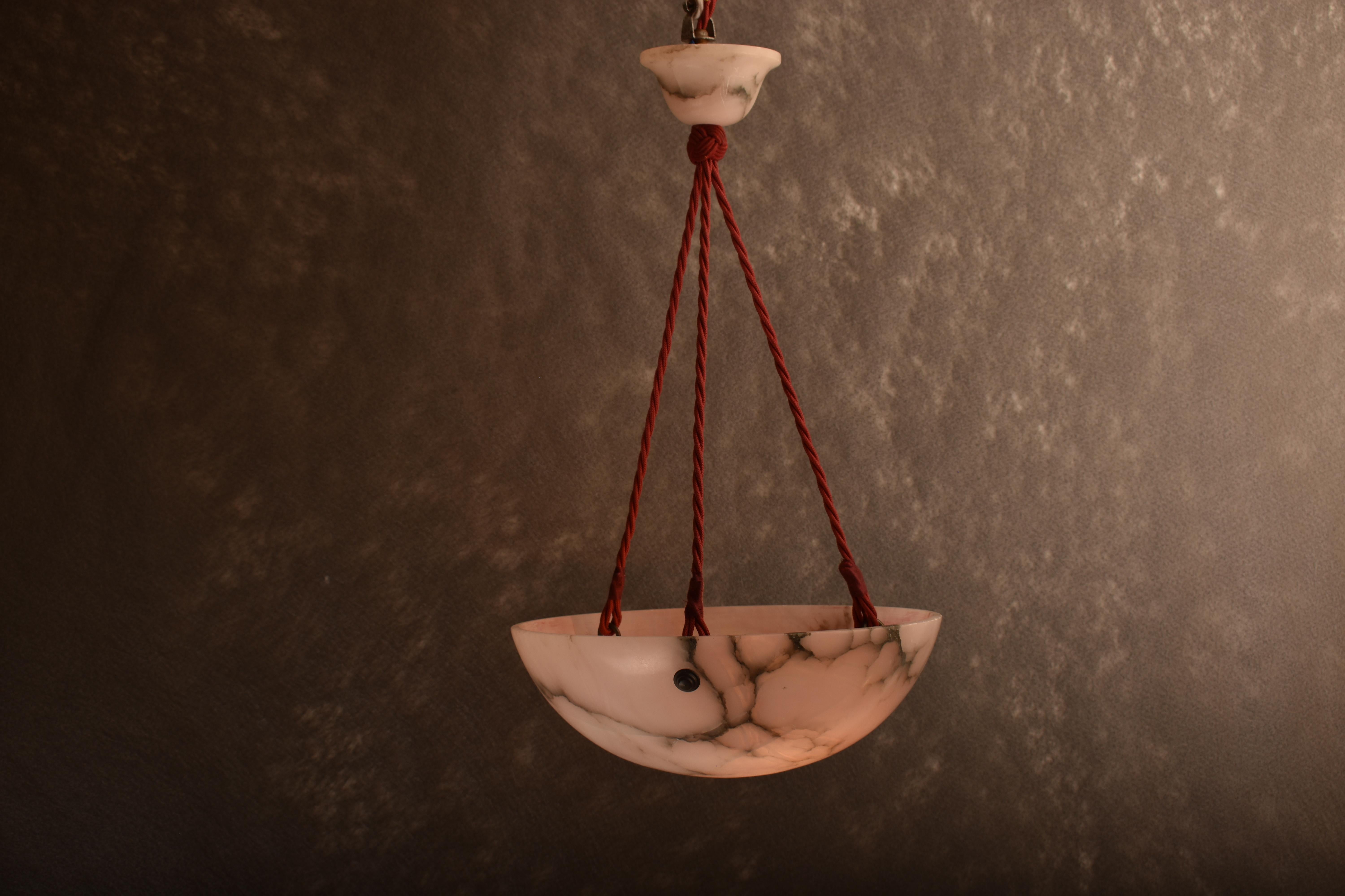 Natural art deco pink toned alabaster pendant lamp. 
It was  hand carved in Switzerland in the early decades of last century.
The lamp has an attractive pink to Sienna veining, giving a comfortable and soft lighting. 
Suspended on three ropes from a