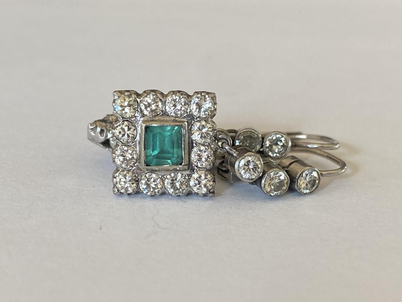 A pair of vintage drop down earrings each feature a natural green Colombian emerald-cut emerald at the center surrounded by a halo of Old European cut diamonds totaling approximately 1.50 carats, F color, VS2 clarity and fashioned in 18kt white