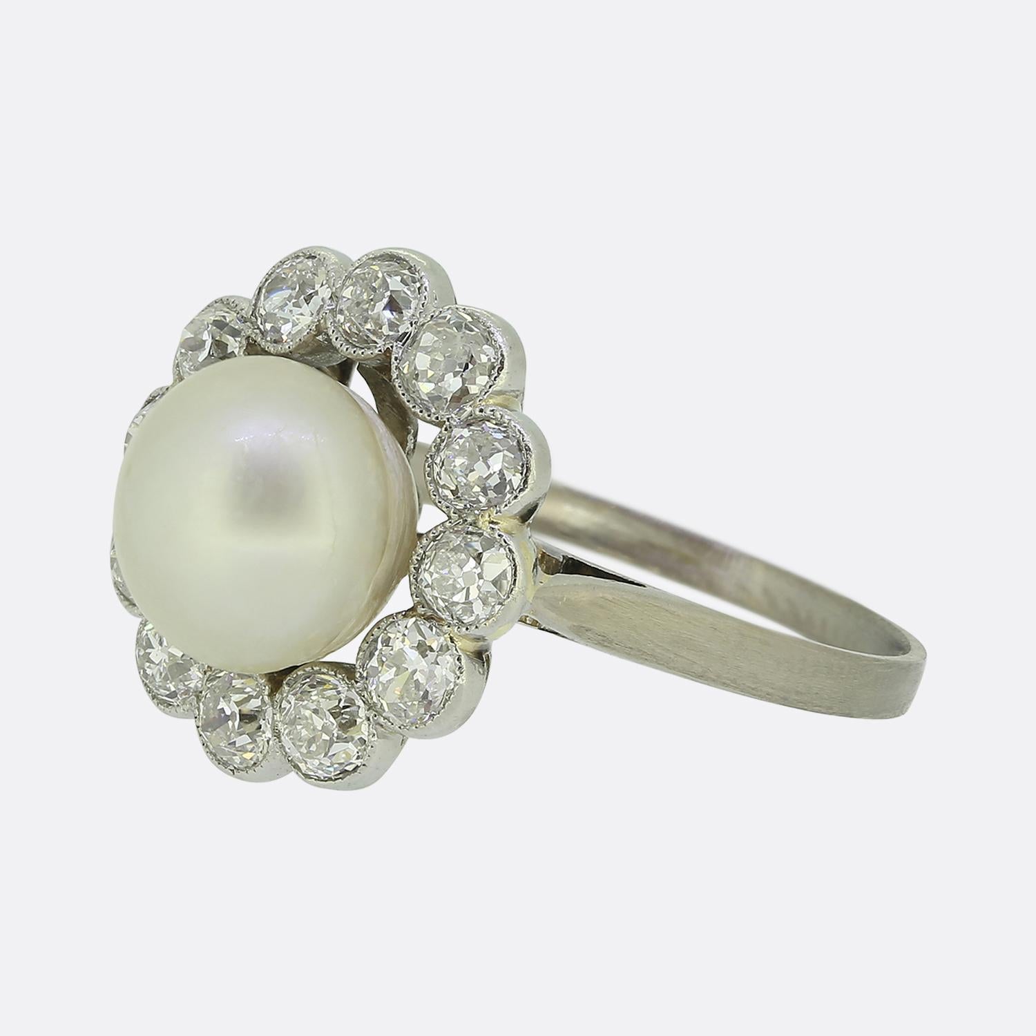 Nous avons ici une exquise bague à grappes de style Art déco. Réalisée en platine, cette pièce raffinée met en valeur une perle blanche centrale, parfaitement ronde et brillante. Cette pierre principale naturelle est entourée d'un cadre de diamants