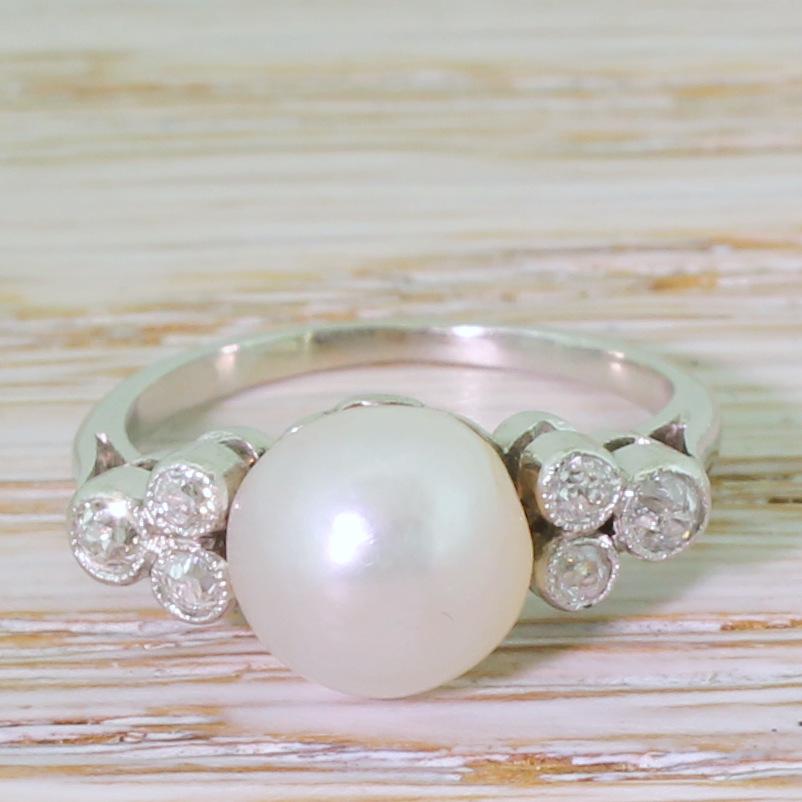 A simply vintage pearl ring. The natural (not cultured) saltwater – and very slightly button shaped – pearl displays a lovely cream lustre, and is flaked either side by three (six total) high white gold cut diamonds in a trefoil formation. The pearl