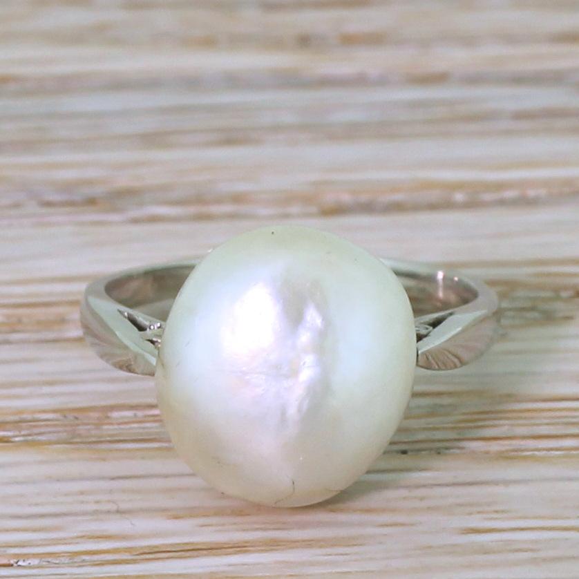 An impressively large and lustrous natural saltwater pearl in a simple, classic setting. Secured in a fine platinum mounting with a scalloped “cup,” with diamond set cheniers under the shoulders, to a slim platinum shank.

Accompanied by a pearl
