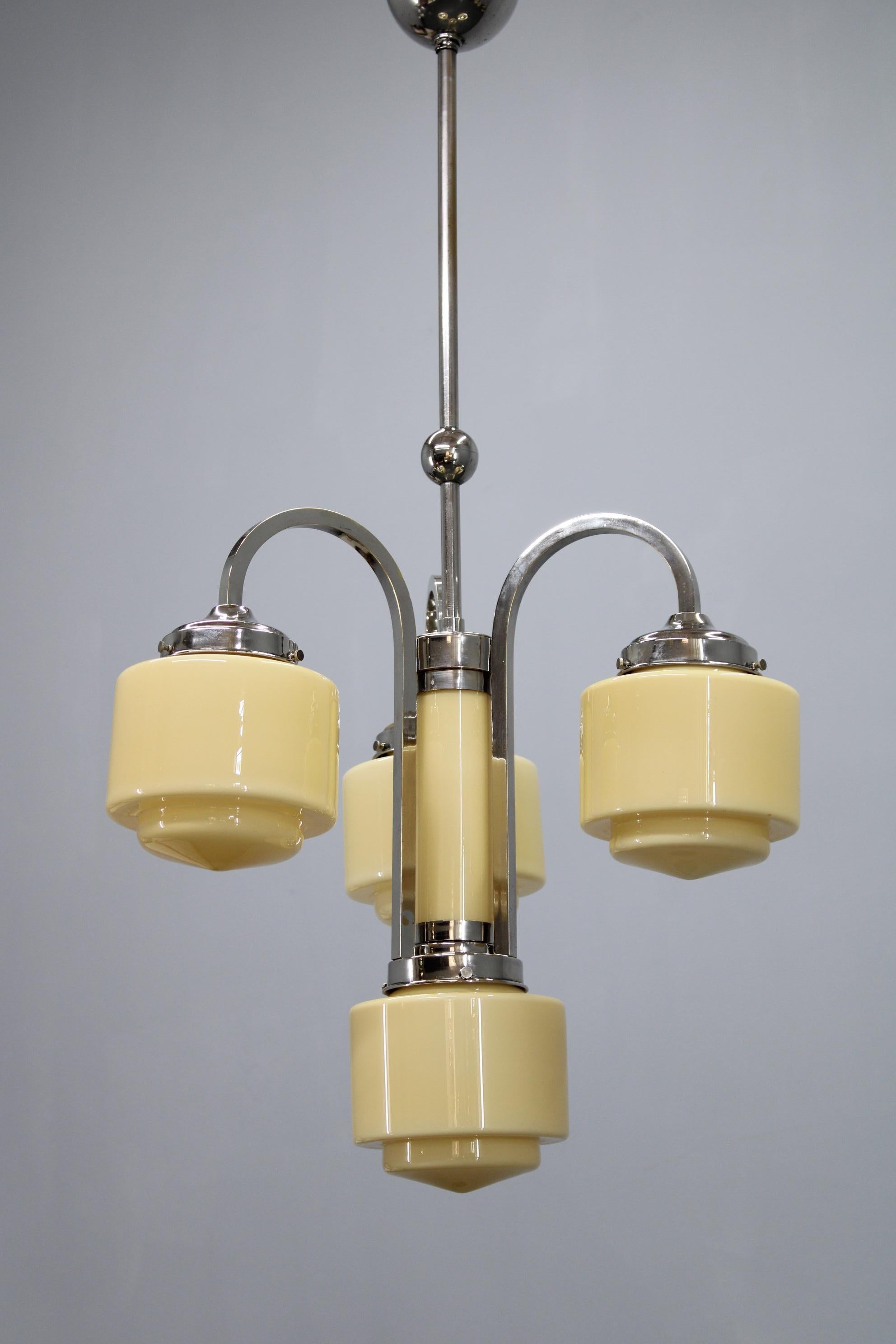 Elegant Art Deco chandelier manufactured in Czechoslovakia in the 1930s, composed of a nickel-plated metal structure, four cream-colored cylindrical glass shades, and a matching central glass cylinder column. The curved arms and geometric