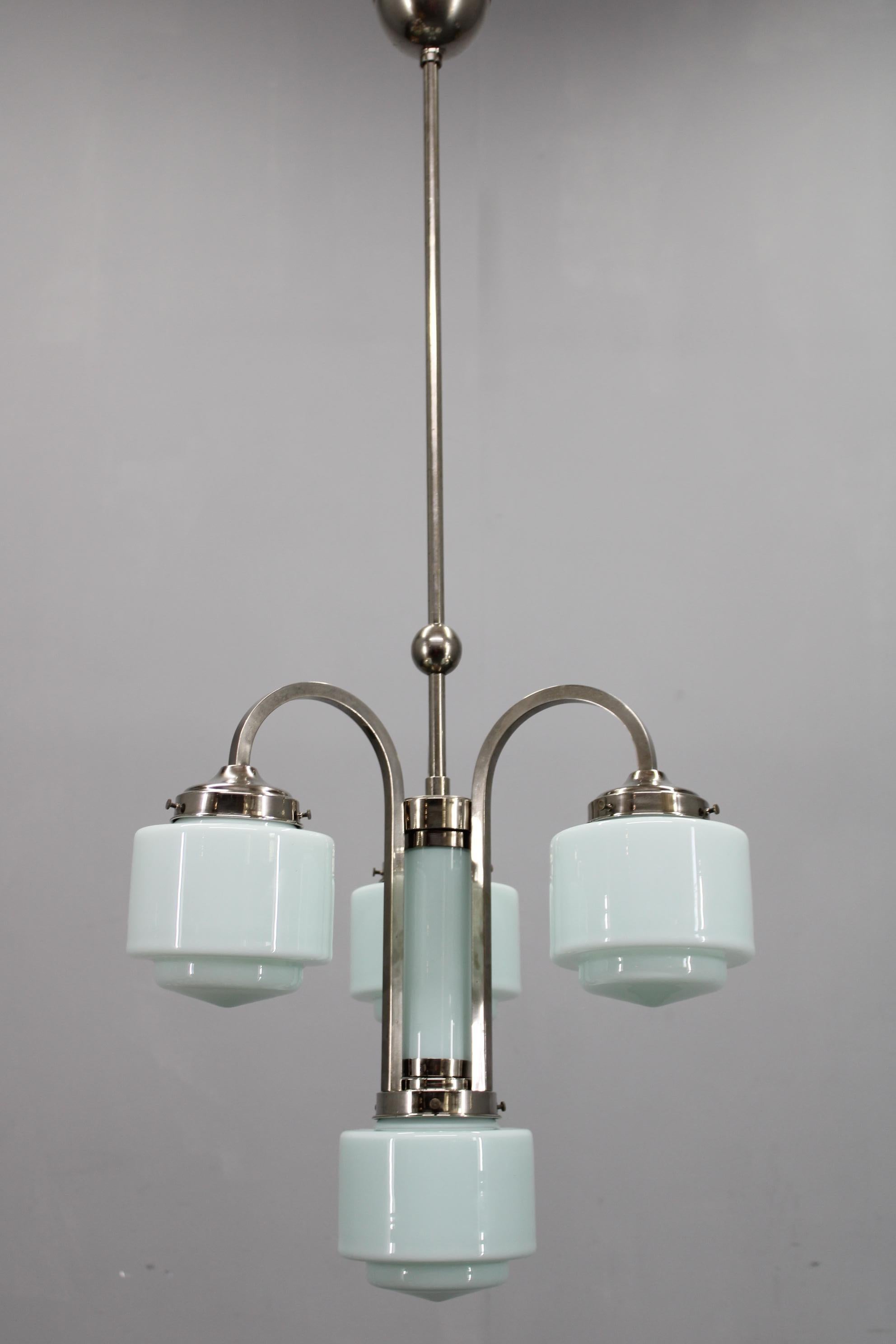 Elegant Art Deco chandelier, produced in Czechoslovakia in the 1930s, constructed from nickel-plated metal and featuring four cylindrical opaline light blue glass shades arranged around a central cylindrical glass column. The soft pastel color and