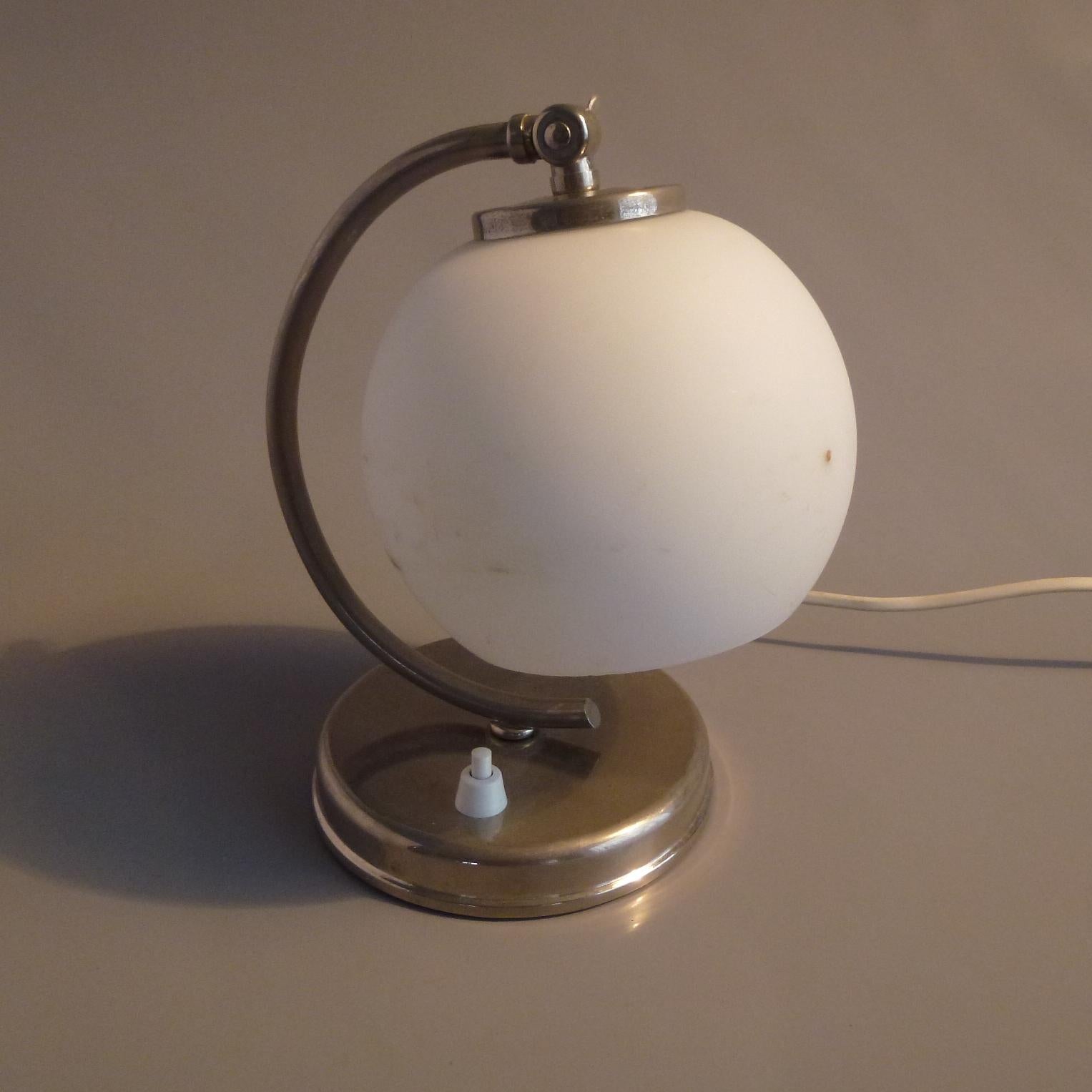 Art Deco table lamp in nickel-plated brass and milk glass sphere shade.
The lamp can be used as wall light too.
European one light bulb socket E27 compatible with UK and US standards.
European 2 pin plug.