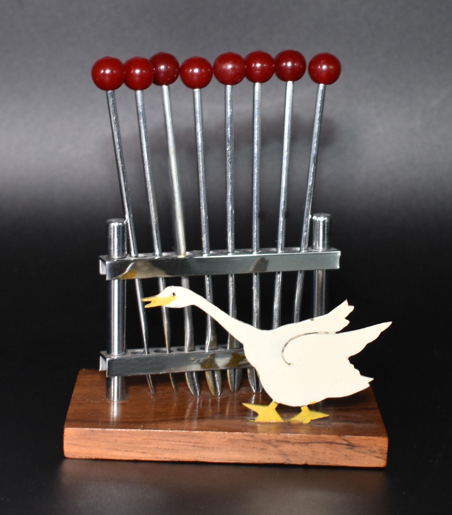 A novelty 1930s cocktail stick set in the manner of a goose, made in France. Features cherry red coloured Bakelite cocktail sticks with chromed metal prongs, all contained within a chrome box hold on a walnut base. Great set in very good condition,