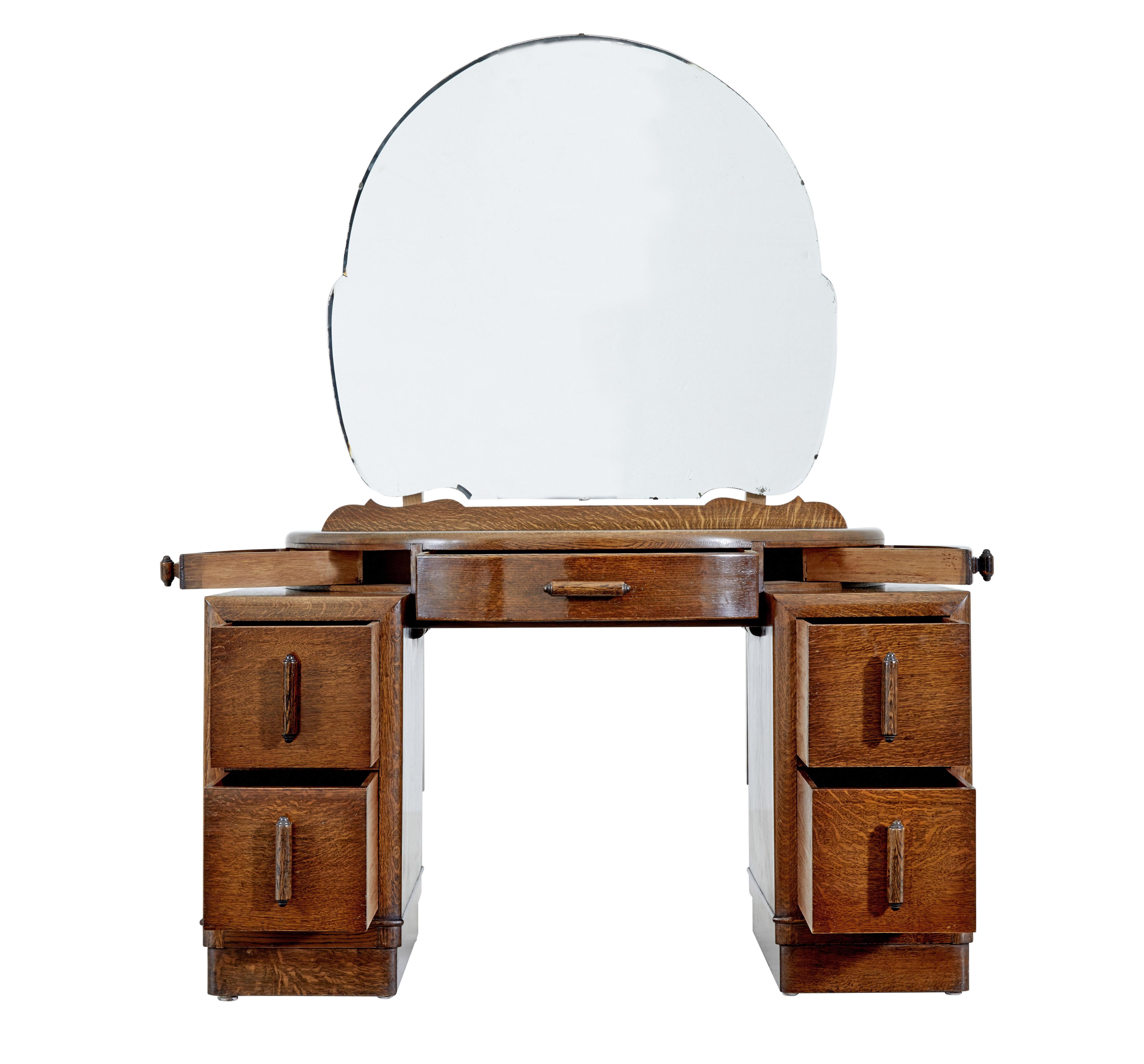 Art Deco oak dressing table with mirror circa 1930.

English made by Sheard Binnington and co of doncaster.  Shaped mirror with bevelled edge which fixes to the demi lune top surface which features a drawer above the knee and 2 swing out