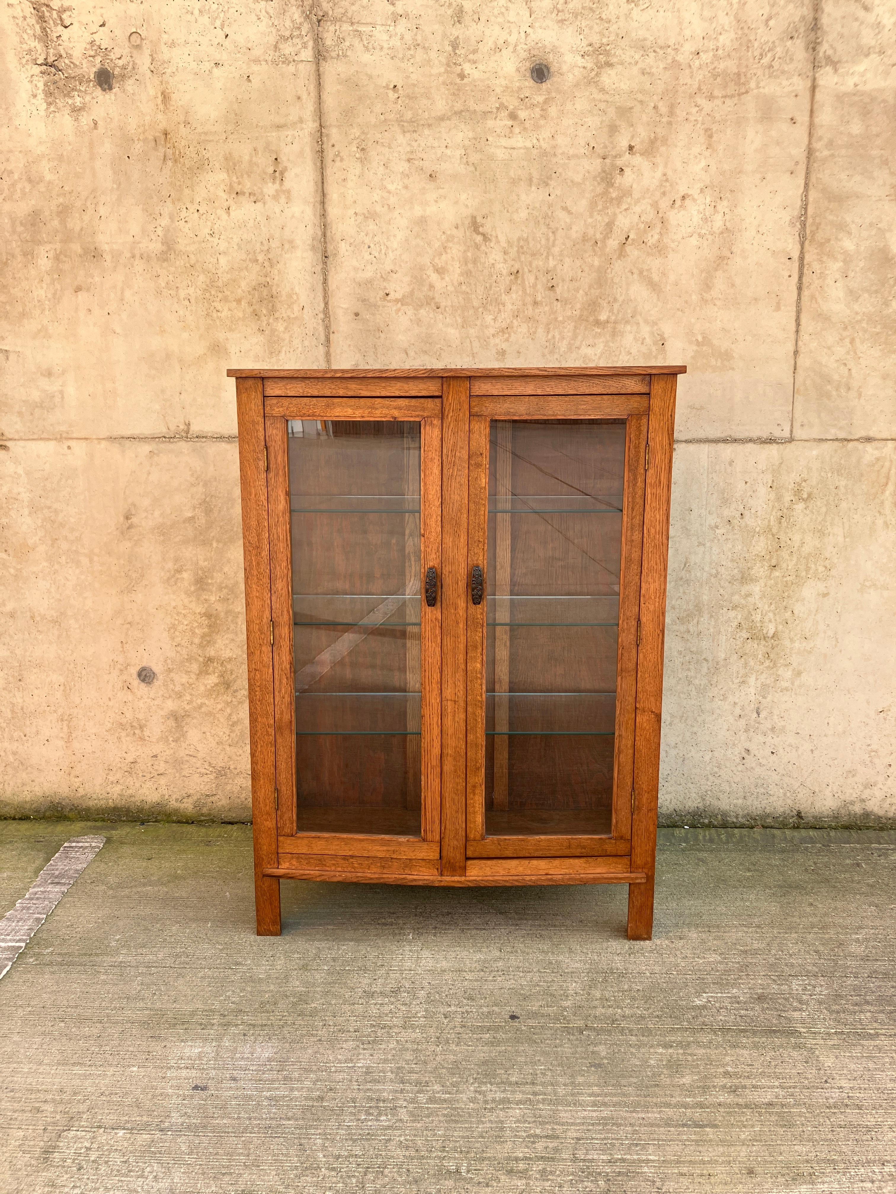 A stunning English Art Deco cabinet. The glazed antique cabinet has glass shelves for displaying items. Beautiful Art Deco handles. The cabinet is a lovely shape and size; the front has a slight triangular shape to it. The oak has plenty of