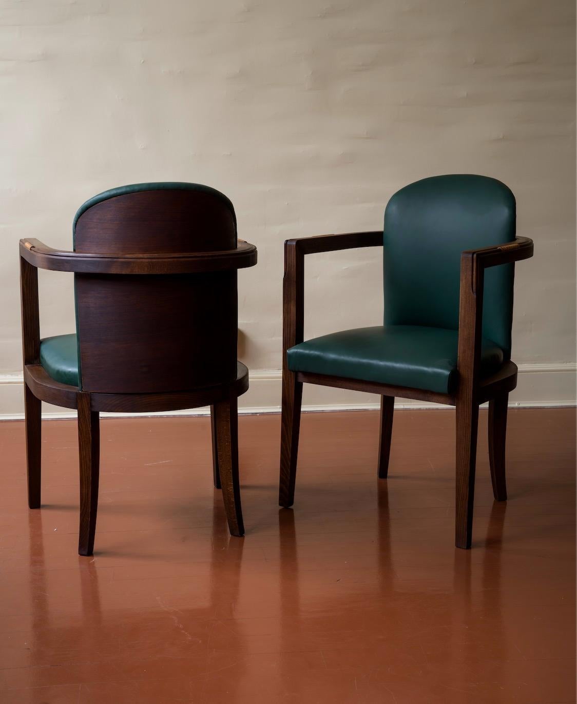 A pair of Art Deco oak and leather armchairs, masterfully blending elegance with craftsmanship. The solid oak frames have been recently restored with a satin oil-based finish, enhancing their natural warmth and depth. The armrests feature hand