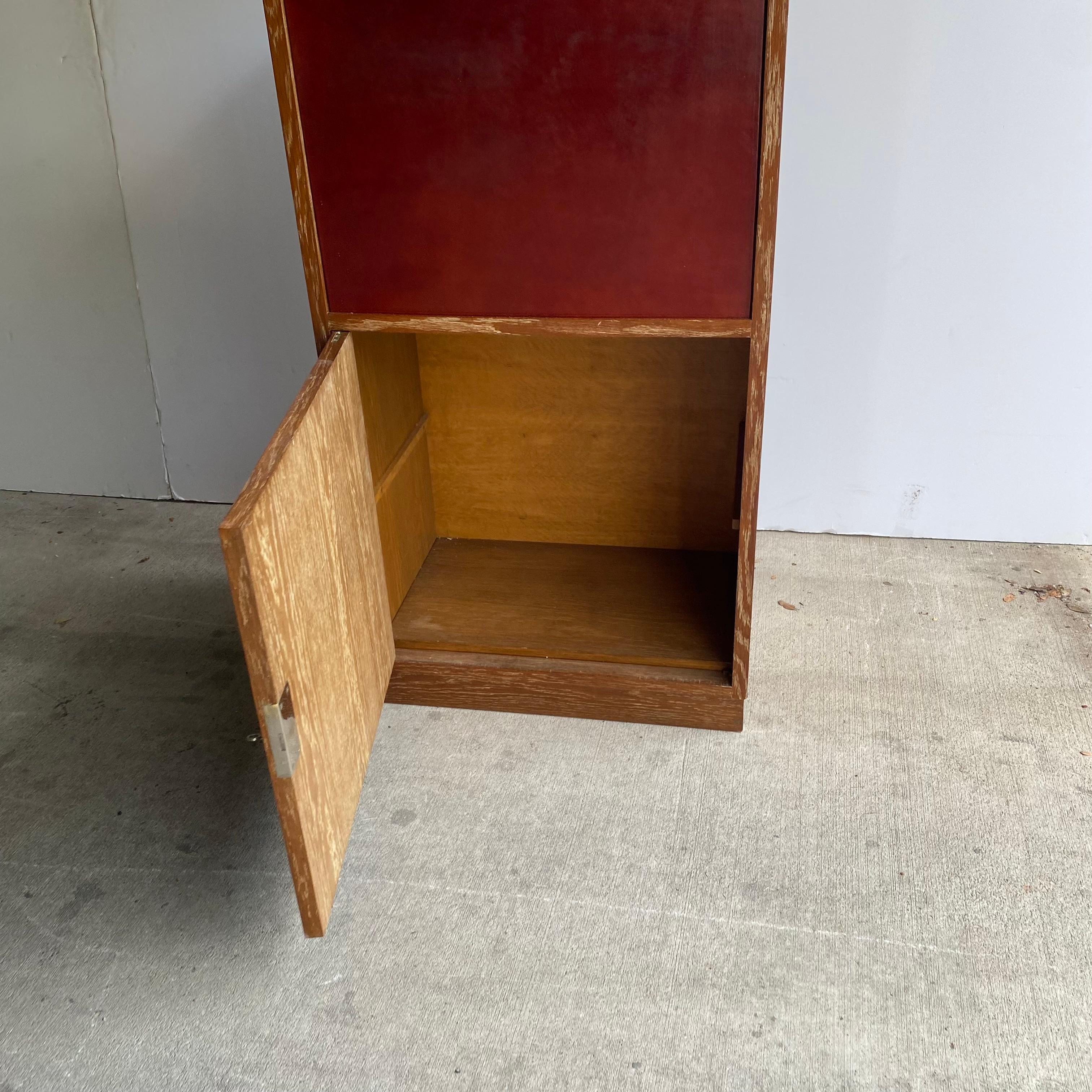 Cerused oak cabinet with oxblood leather-fronted door that drops down to expose secretary work surface with fitted interior including drawers. Heavy cast hardware and key. A sublime example of early modernist work by Charles Dudouyt. France, 1930's.