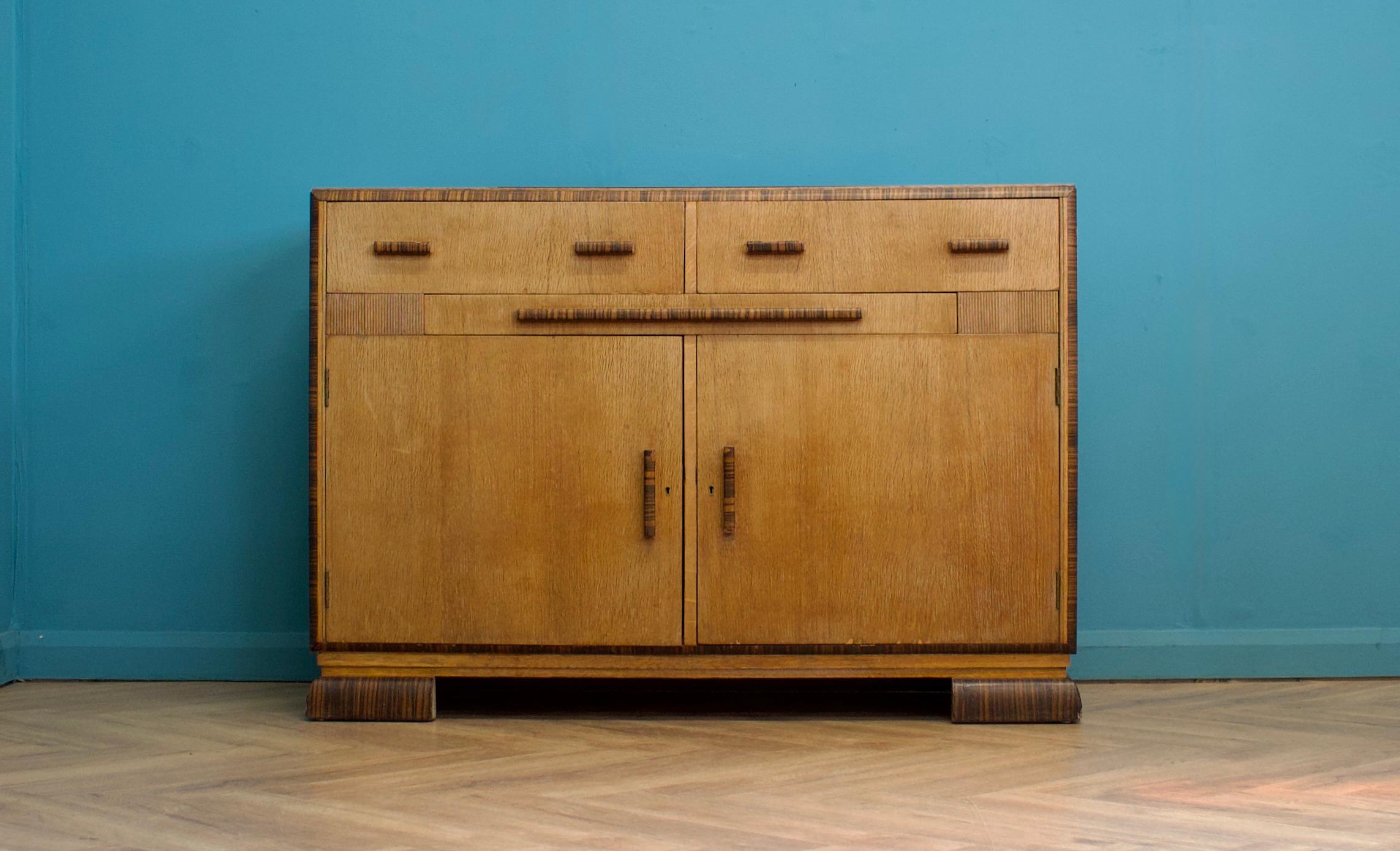 This high-quality oak Art Deco sideboard, circa 1930s, features a cupboard with shelves, two drawers, and a pull-out shelf with a compartment for additional storage.
