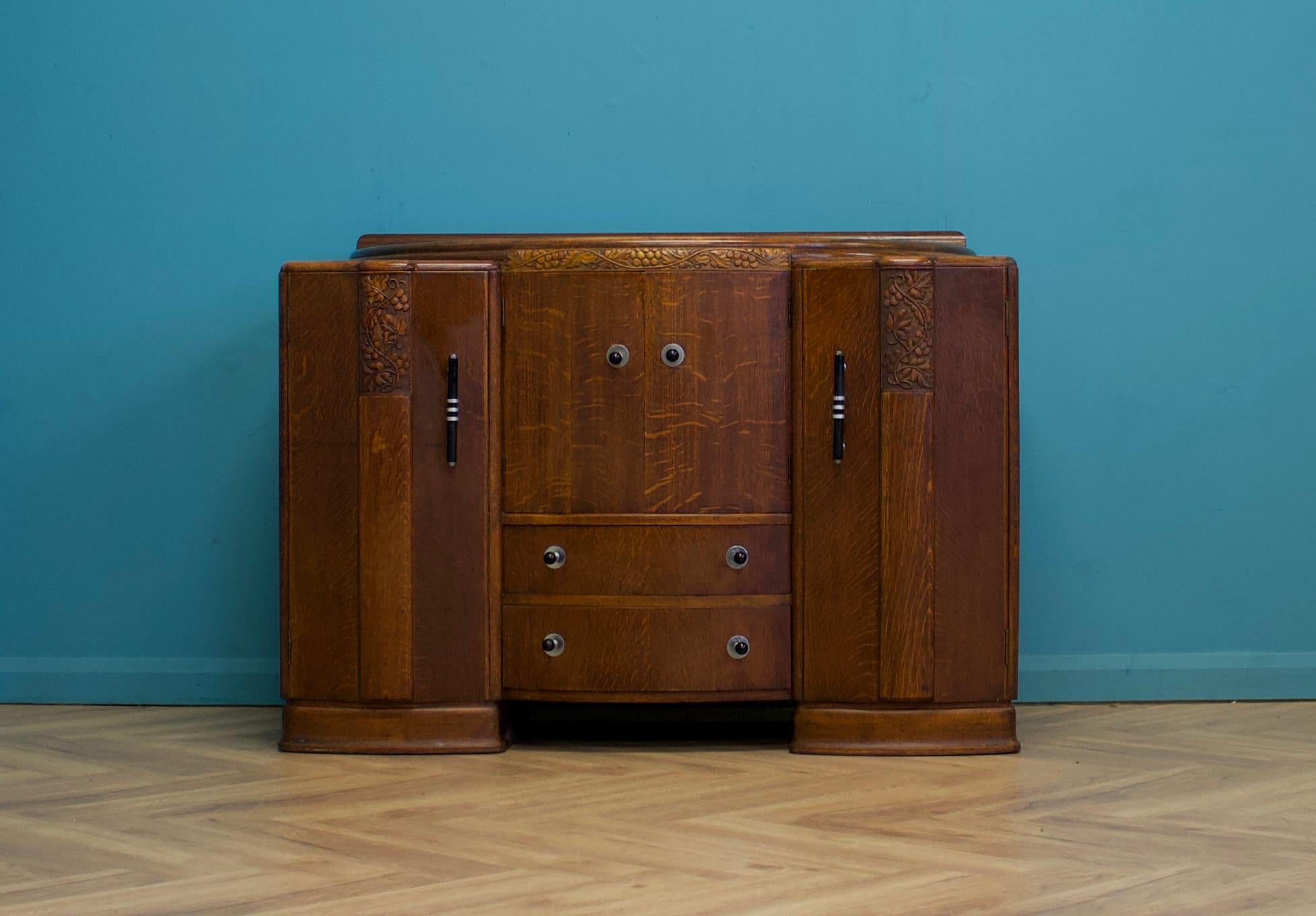 This high-quality dark oak Art Deco sideboard, circa 1930s, features two cupboards, each with shelves. One cupboard has an additional drawer, while the middle cupboard contains a drinks cupboard with two drawers underneath.
